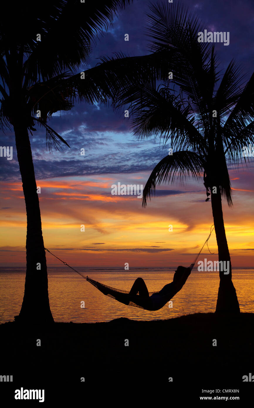 Woman in hammock, and palm trees at sunset, Coral Coast, Viti Levu, Fiji, South Pacific Stock Photo