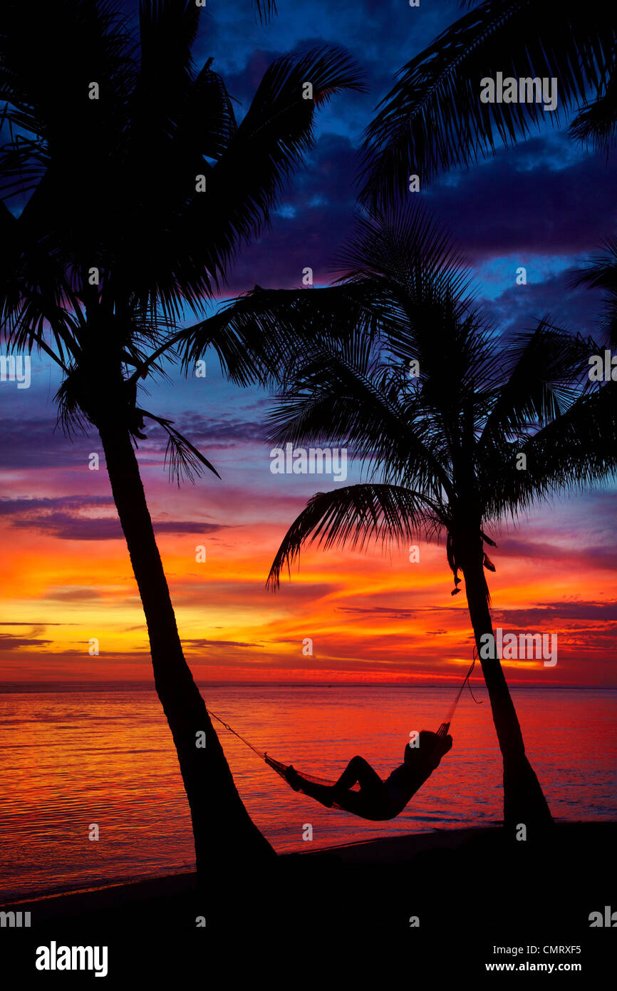 Woman in hammock, and palm trees at sunset, Coral Coast, Viti Levu, Fiji, South Pacific Stock Photo