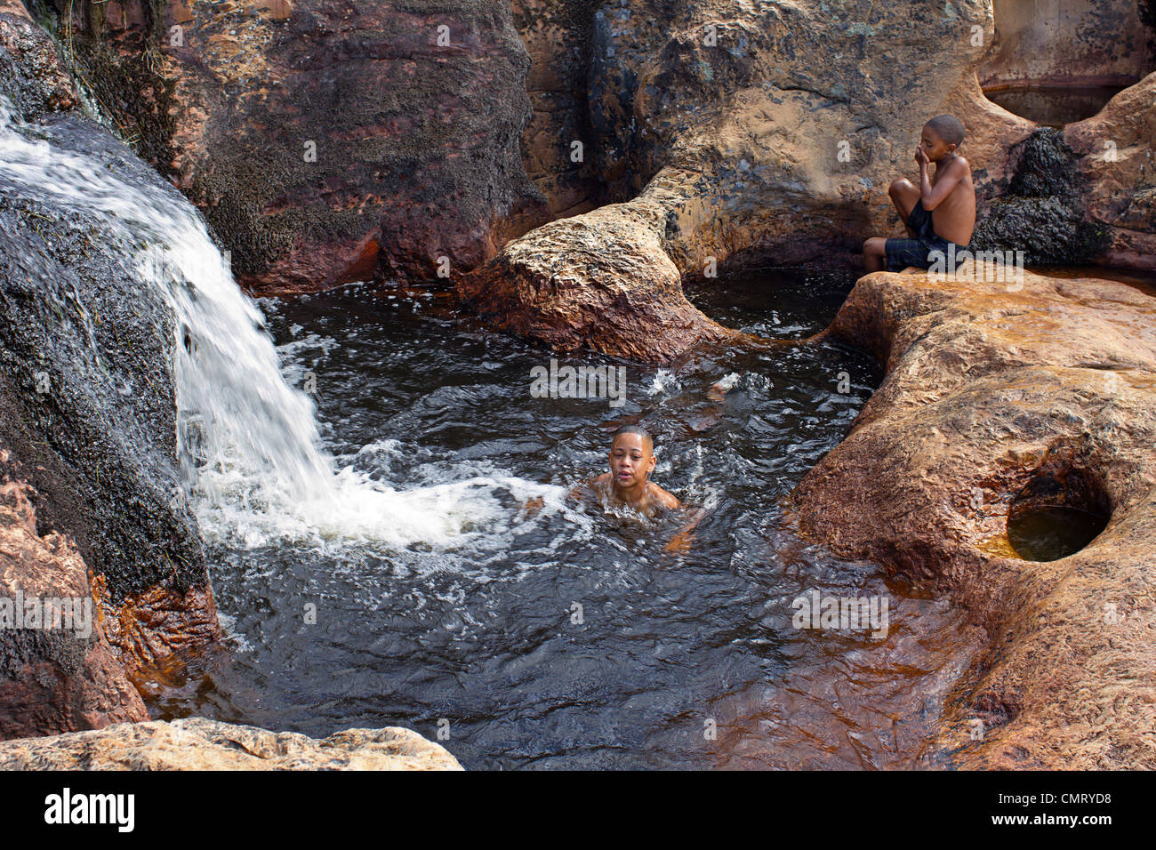 3 young South African children swimming in a rock pool beside a waterfall Stock Photo