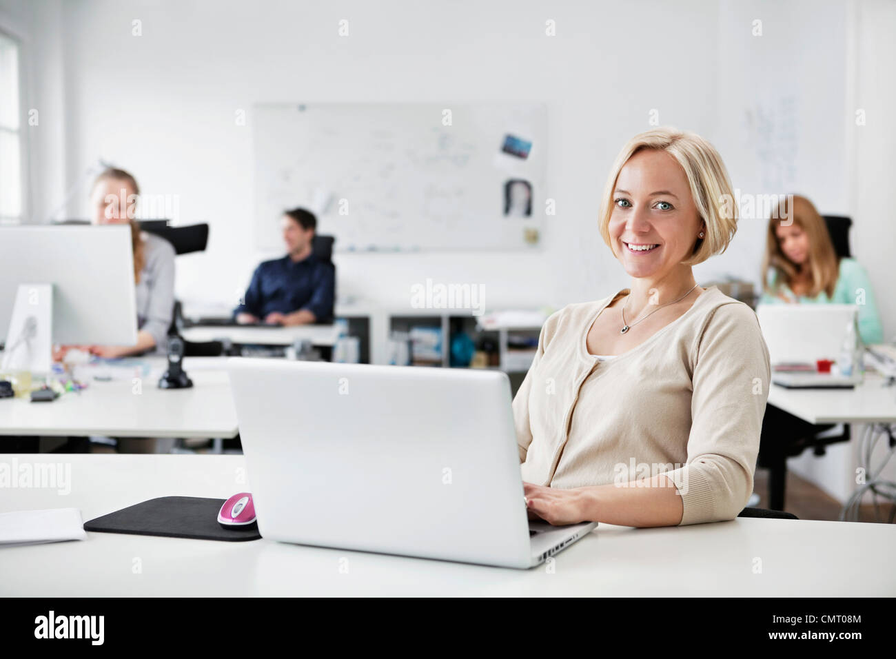 Woman sitting by computer with people in the background Stock Photo
