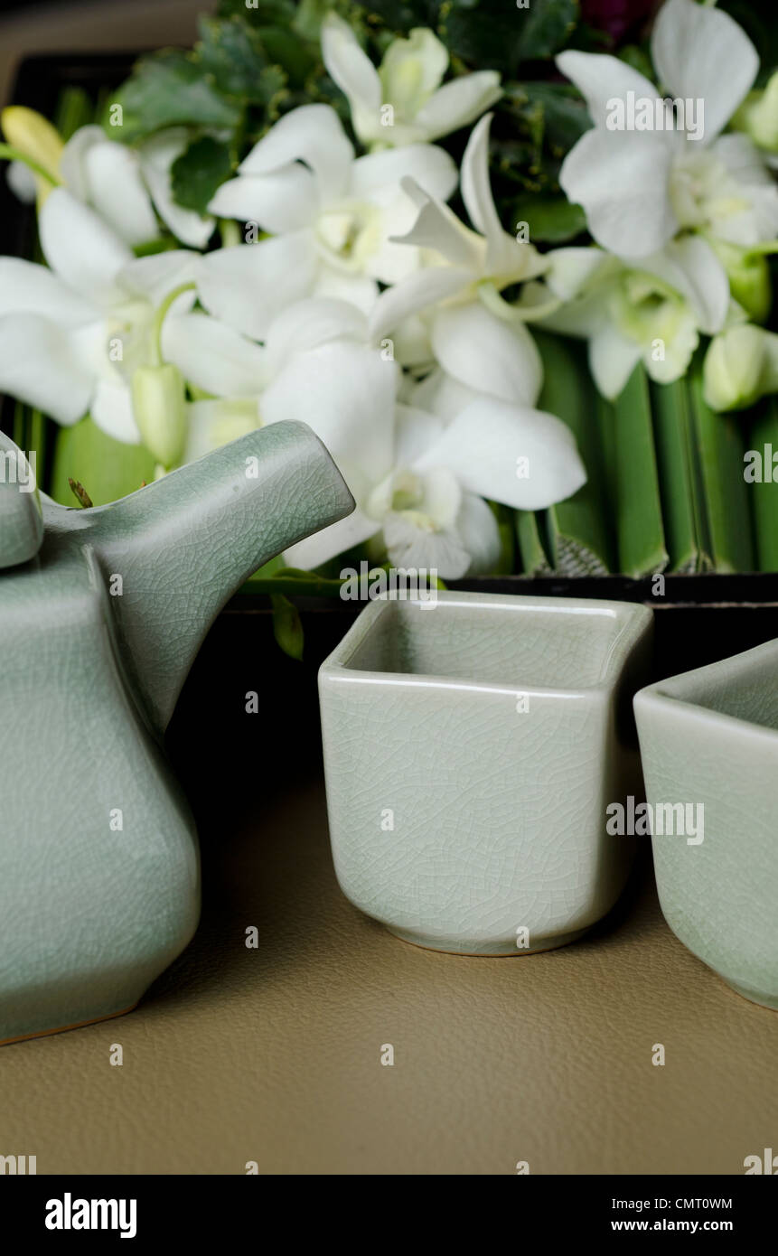 Thailand, Bangkok. Traditional Thai tea pot and cups with orchid arrangement. Stock Photo