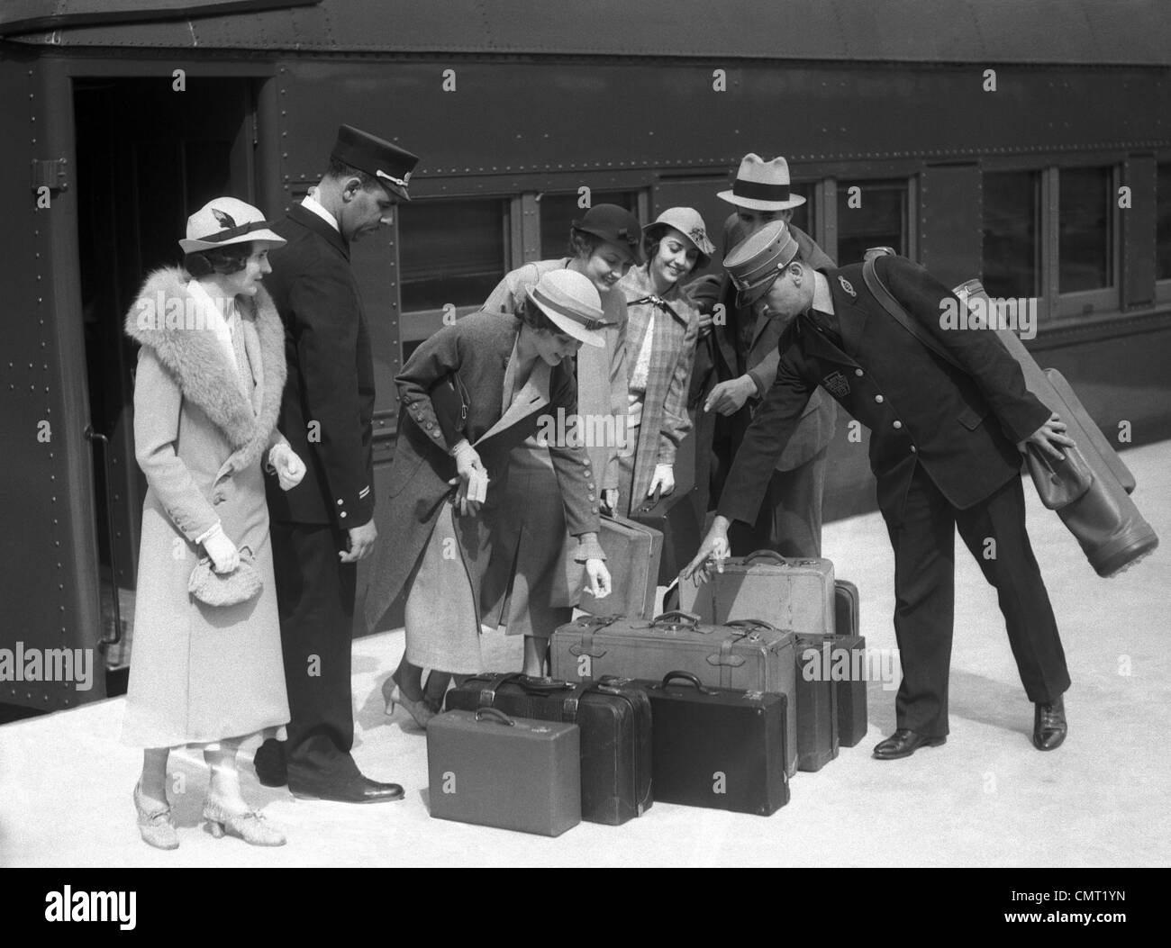 1920s 1930s TRAVELERS ON TRAIN PLATFORM IDENTIFYING LUGGAGE FOR PORTER Stock Photo