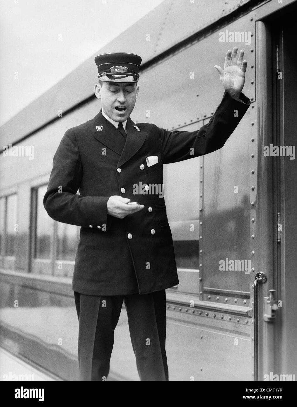 1930s CONDUCTOR MAKING FINAL BOARDING CALL OUTSIDE TRAIN Stock Photo