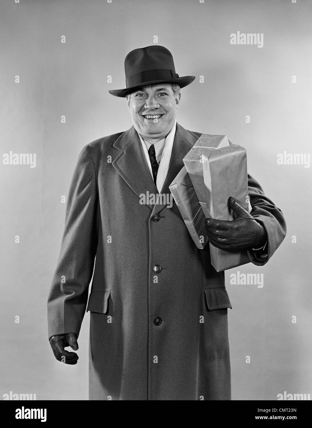 1940s 1950s SMILING MAN CARRYING SHOPPING BOXES WEARING HAT COAT GLOVES LOOKING AT CAMERA Stock Photo