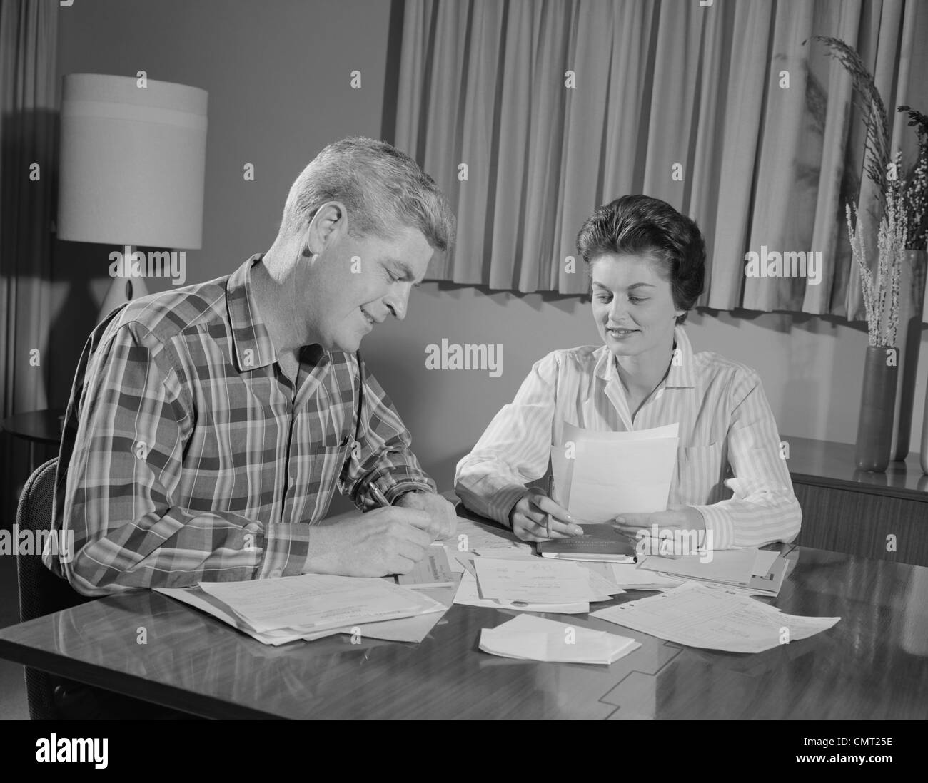 1960s COUPLE MAN WOMAN AT TABLE WORKING ON HOUSEHOLD ACCOUNTS BILLS Stock Photo