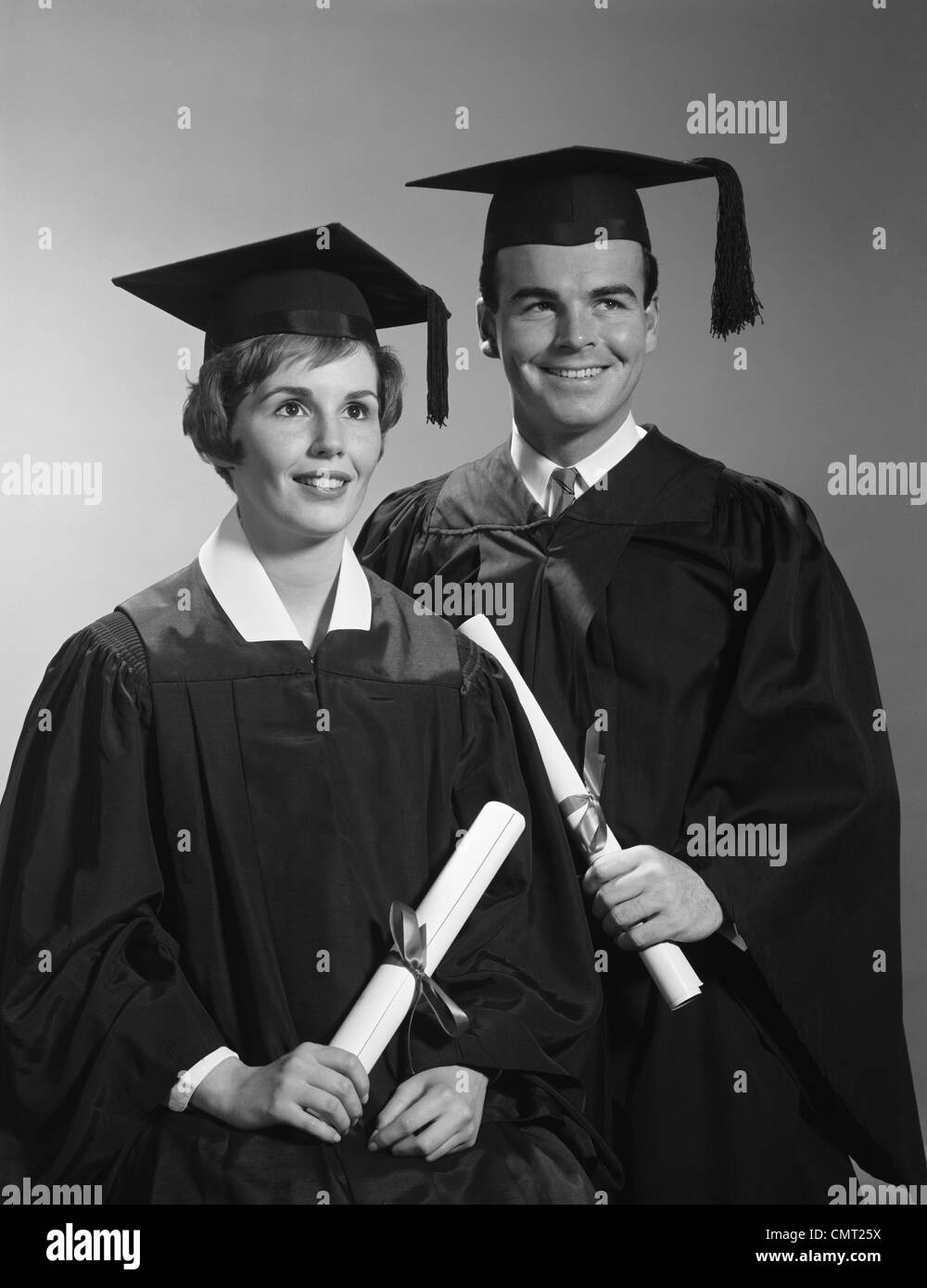 1960s PORTRAIT COUPLE MAN WOMAN IN GRADUATION ROBES HOLDING DIPLOMAS SMILING Stock Photo
