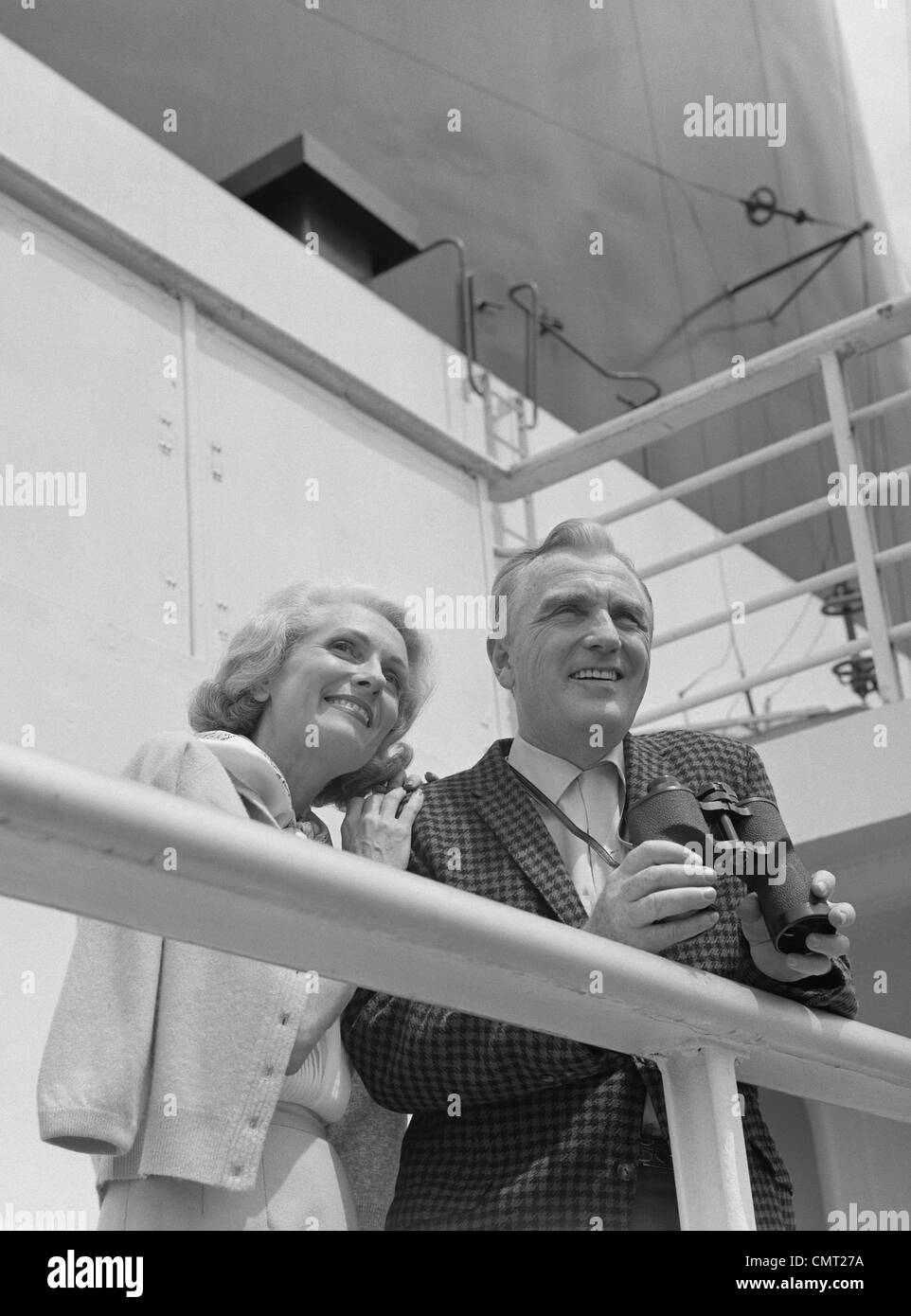 1960s SMILING MATURE COUPLE AT SHIPBOARD RAIL WITH BINOCULARS Stock Photo