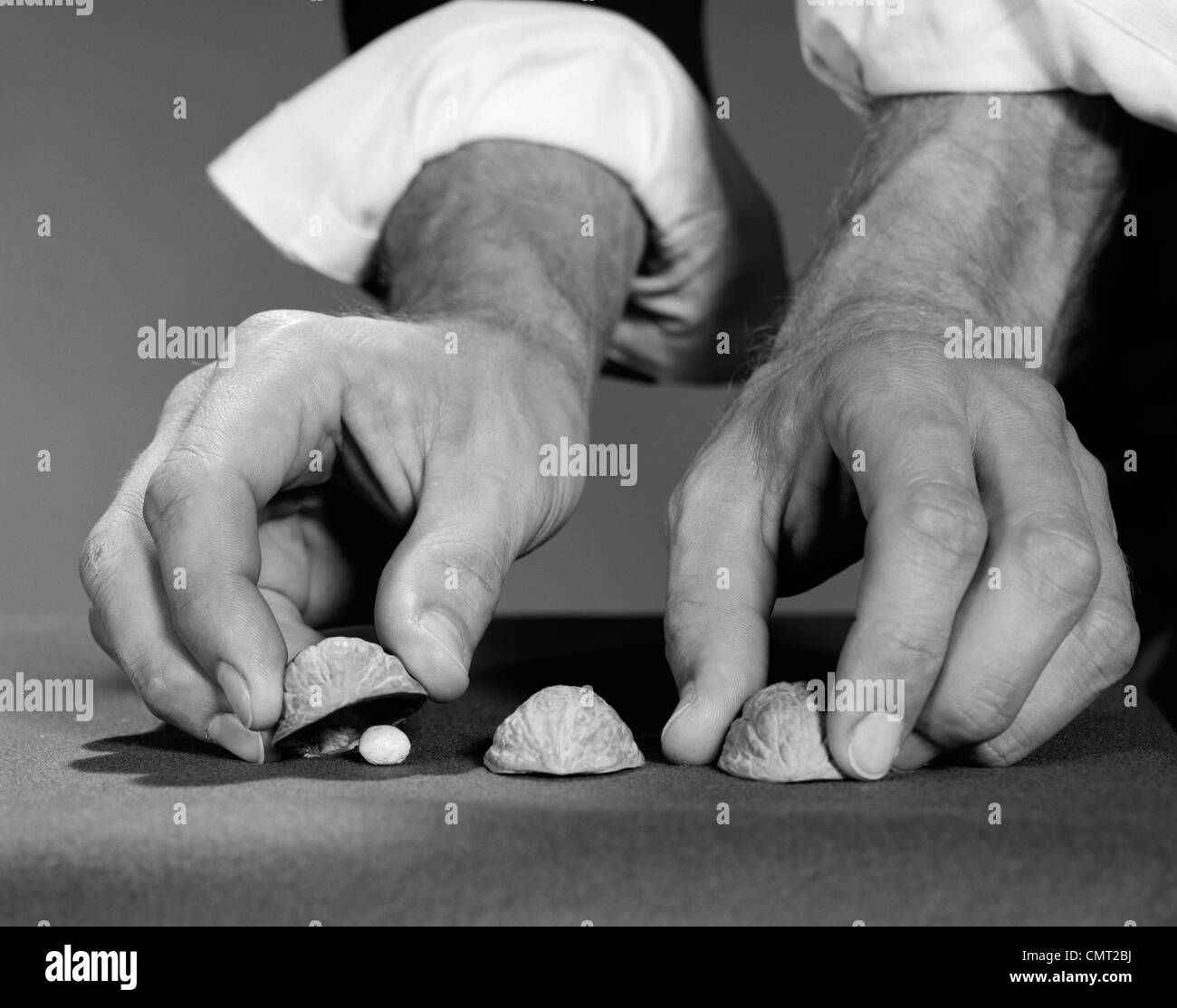 1960s MAN'S HANDS WITH SHIRT SLEEVES ROLLED UP PLAYING SHELL GAME Stock Photo