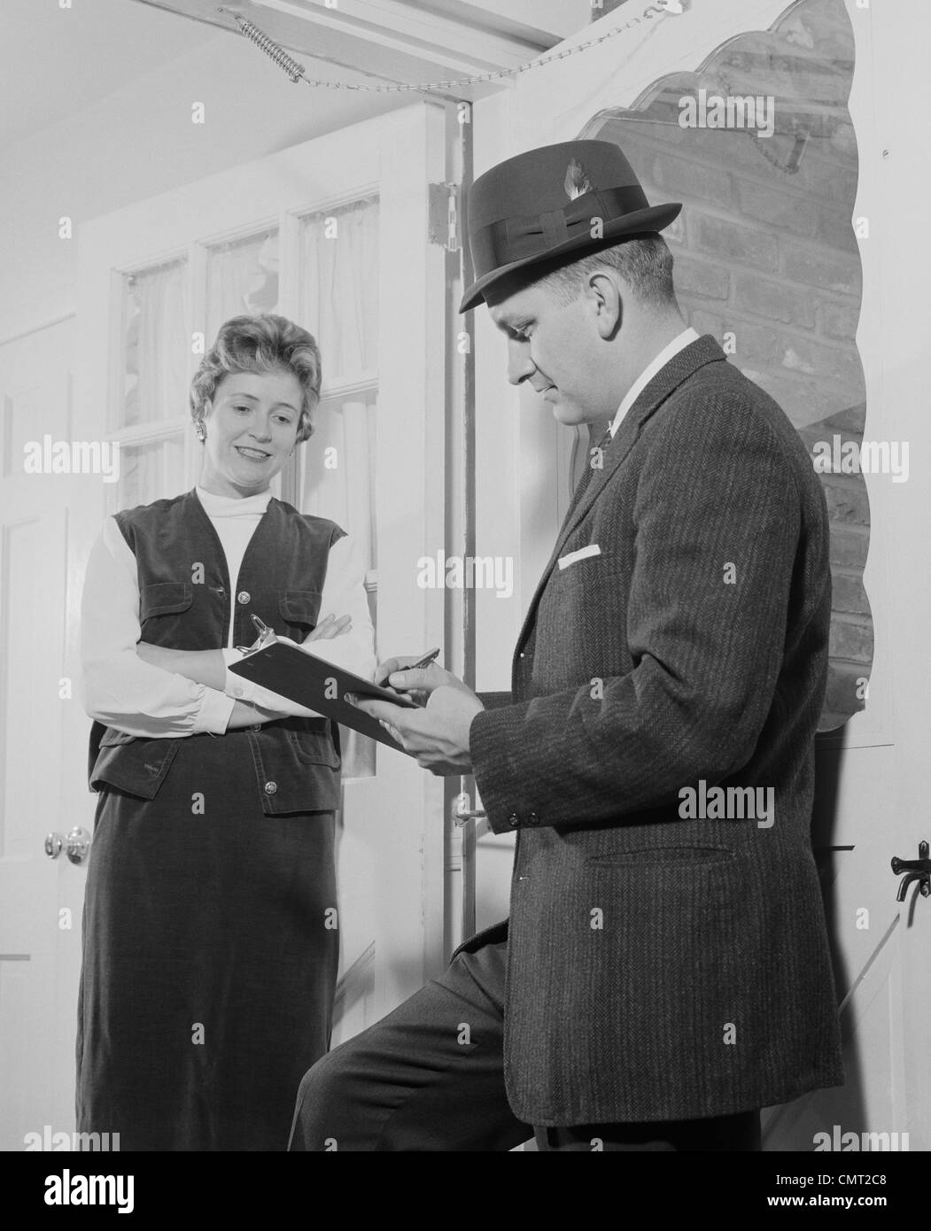 1960s MAN WITH CLIPBOARD TALKING TO WOMAN IN DOORWAY Stock Photo