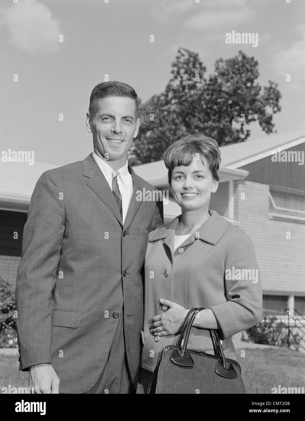 1960s PORTRAIT SMILING COUPLE IN FRONT OF SUBURBAN HOUSE Stock Photo