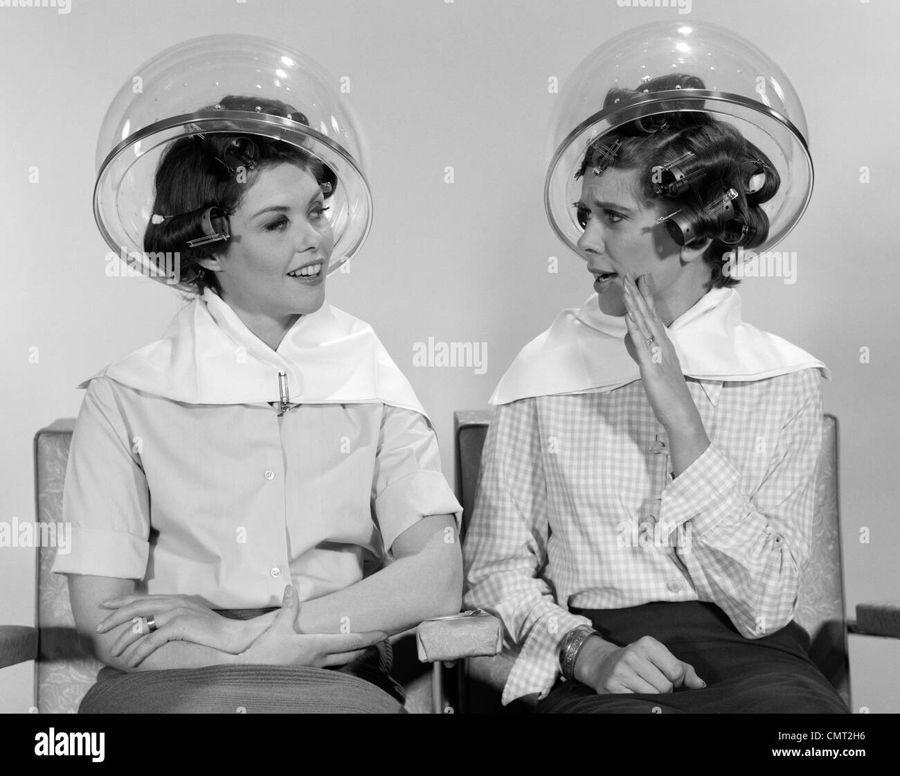 1960s TWO WOMEN SITTING TOGETHER GOSSIPING UNDER HAIRDRESSER HAIR DRYER Stock Photo