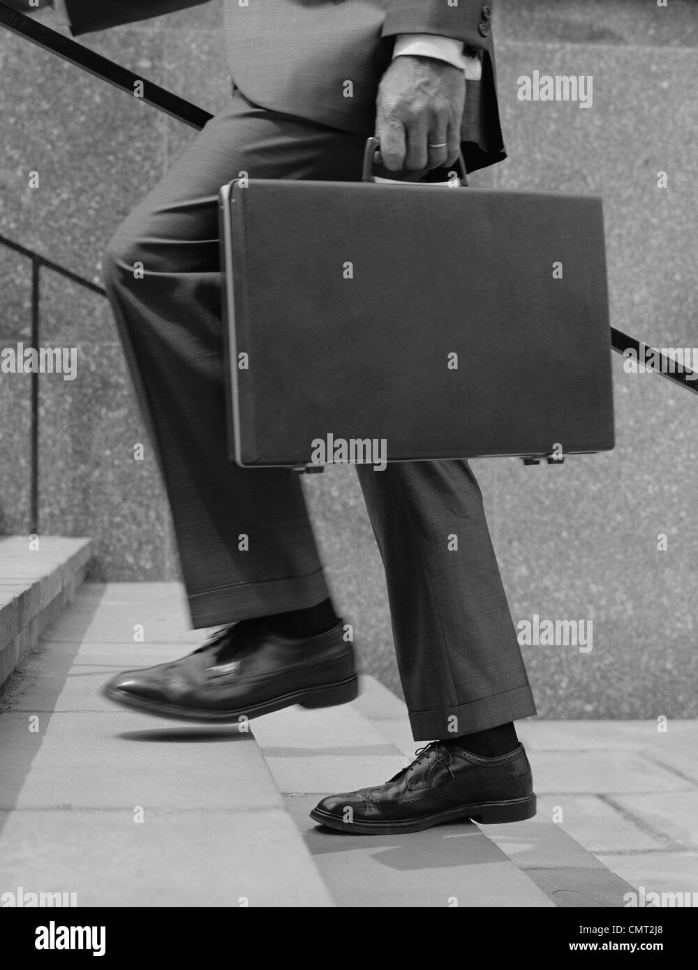 1960s BUSINESSMAN LEGS WALKING UP STAIRS HAND HOLDING BRIEFCASE Stock Photo