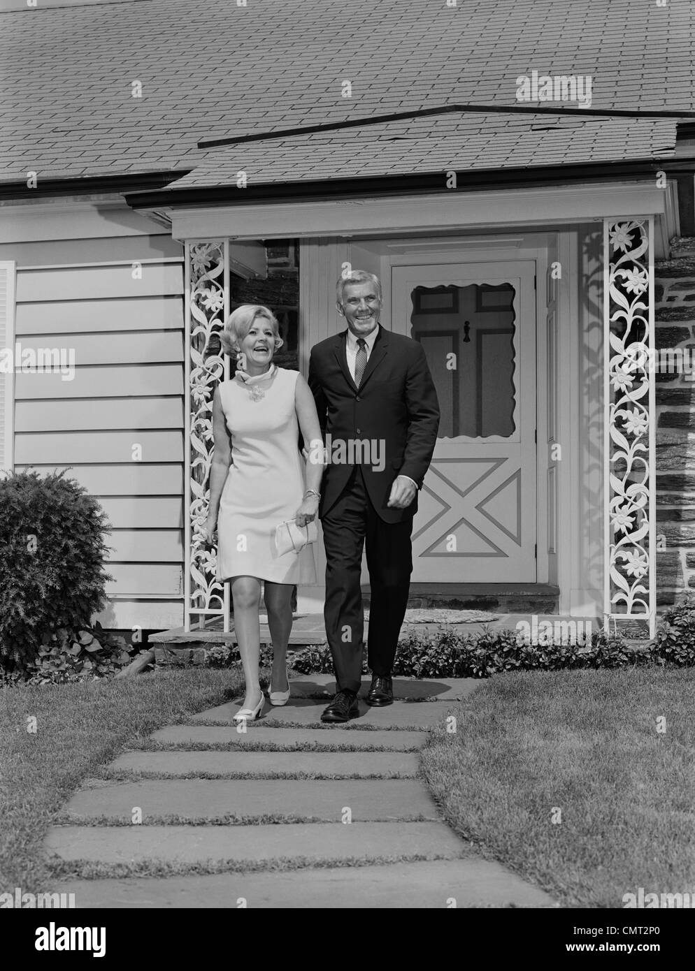 1960s MATURE COUPLE WALKING  ON SIDEWALK FRONT OF HOUSE Stock Photo