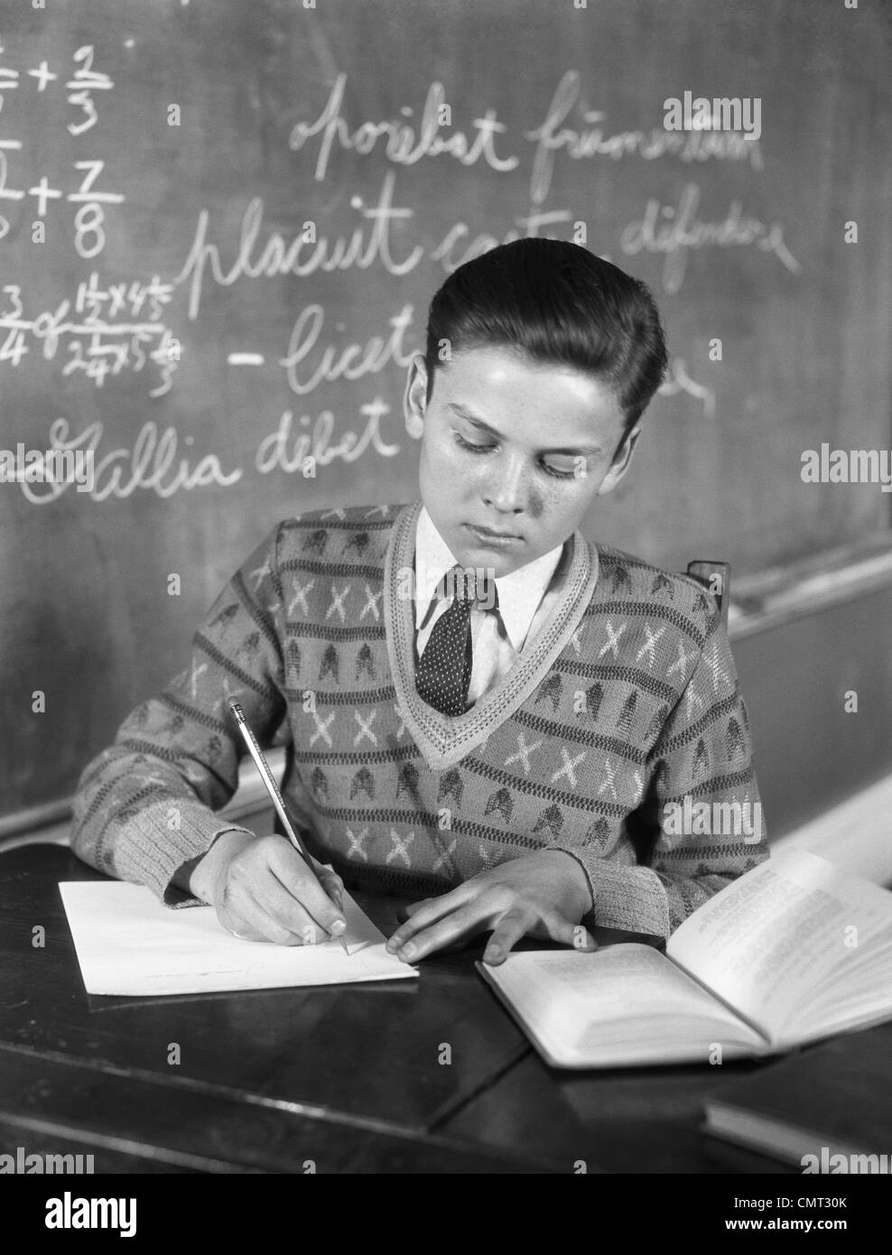 1920s 1930s BOY VEE NECK SWEATER WRITING AT SCHOOL DESK Stock Photo