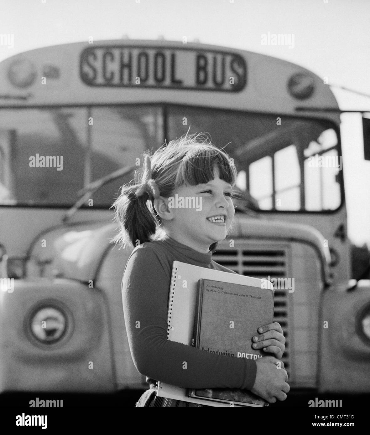 1980s GIRL HOLDING BOOKS STANDING IN FRONT OF SCHOOL BUS Stock Photo