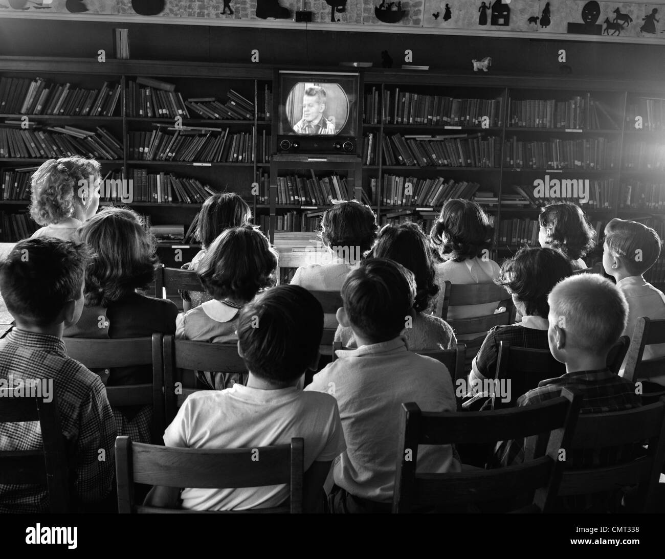 1950s BACK VIEW OF KIDS IN SCHOOL LIBRARY WATCHING TV SCREEN Stock Photo