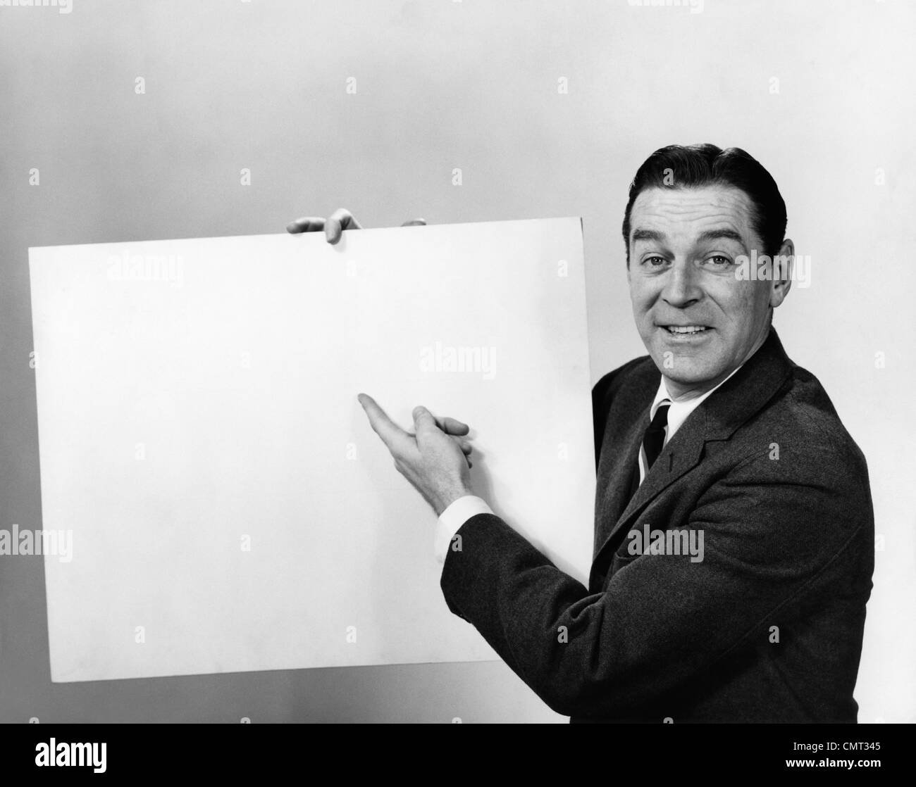 1960s SMILING MAN POINTING TO BLANK POSTER SIGN Stock Photo