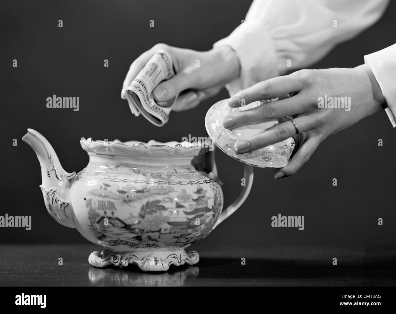 1950s WOMAN'S HANDS PUTTING WAD OF CASH IN TEAPOT Stock Photo