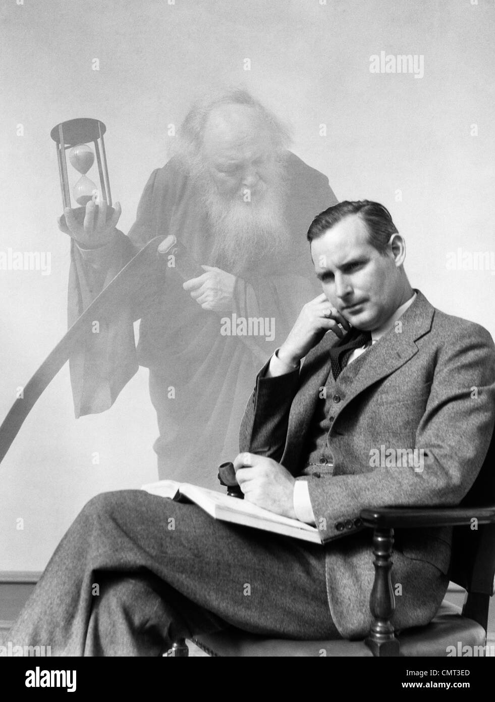 1930s MAN IN SUIT SEATED WITH BOOK IN LAP & PIPE IN HAND WITH PENSIVE LOOK WITH GRIM REAPER GHOSTED IN BACKGROUND Stock Photo