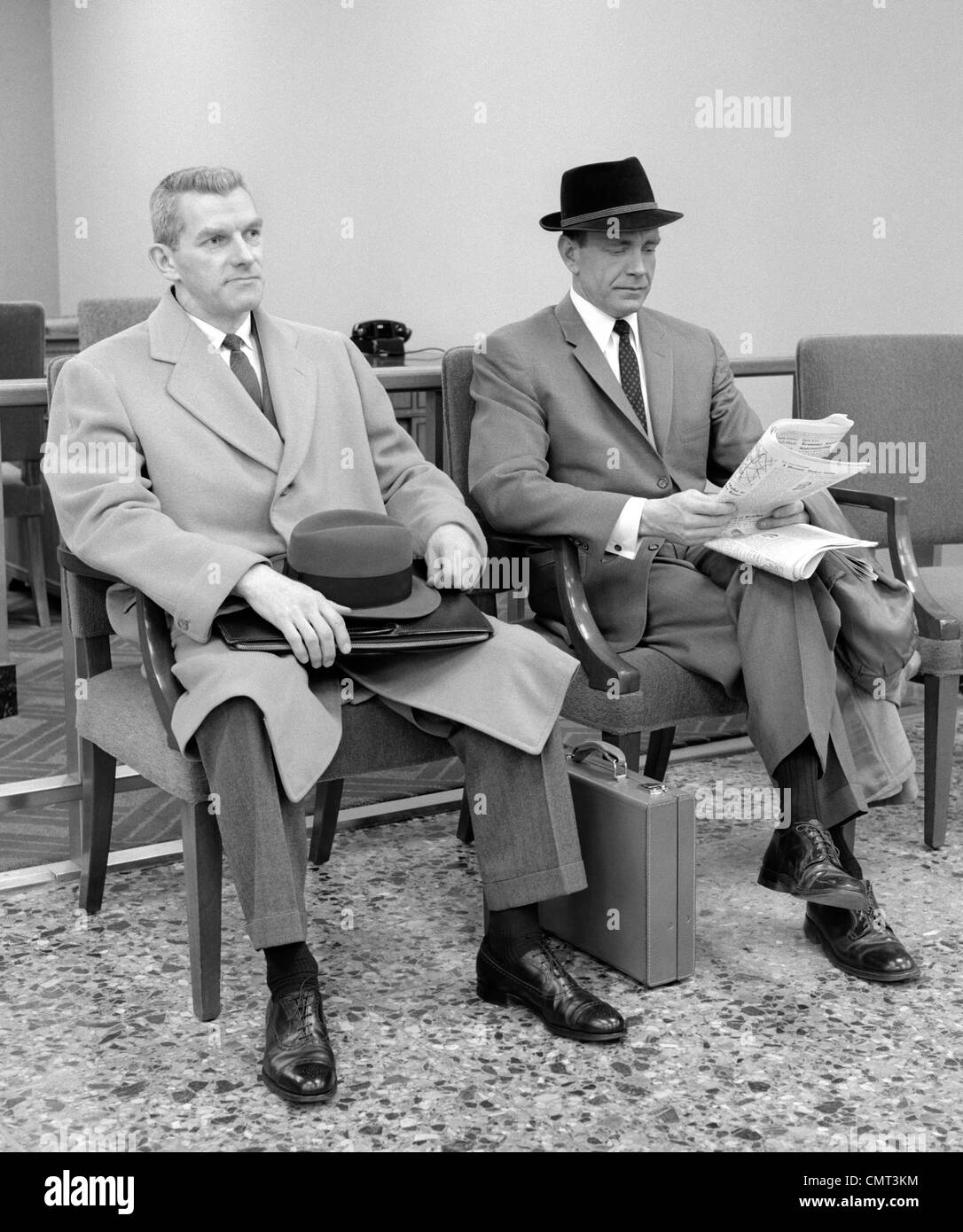 1950s 1960s TWO MEN BUSINESSMAN SALESMAN SITTING IN OFFICE RECEPTION WAITING AREA INDOOR Stock Photo