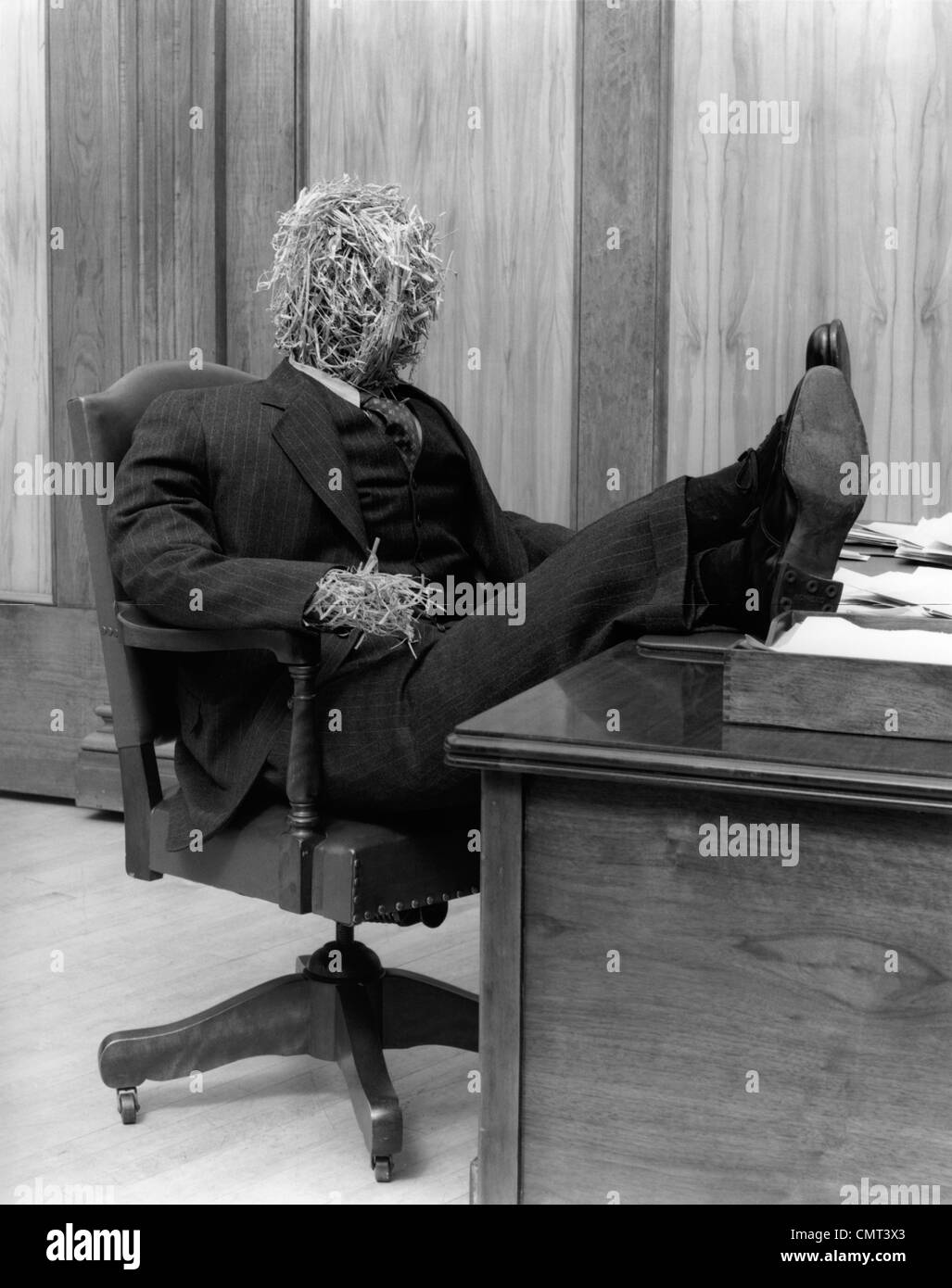 1930s STRAW MAN IN SUIT & TIE SEATED IN EXECUTIVE CHAIR WITH FEET PROPPED UP ON OFFICE DESK Stock Photo