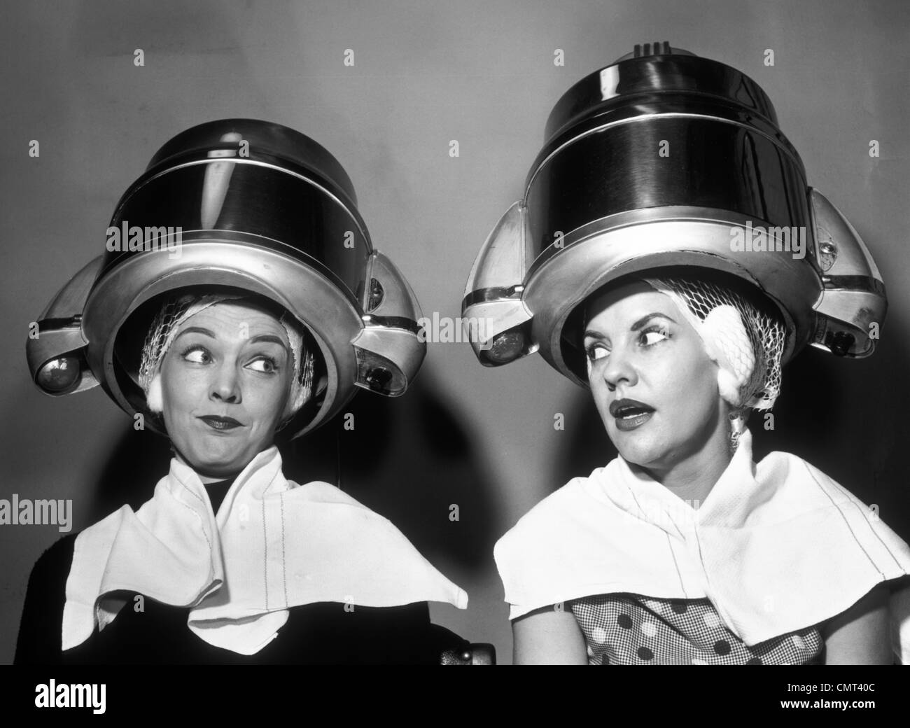 1950s TWO WOMEN SITTING TOGETHER GOSSIPING UNDER HAIRDRESSER HAIR DRYER Stock Photo