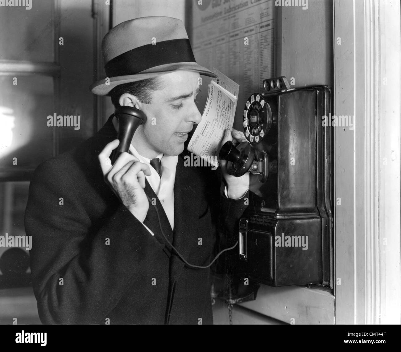 1930s BUSINESSMAN IN HAT AND SUIT TALKING ON PUBLIC PAY TELEPHONE SALES MAN CALLING IN ORDER Stock Photo