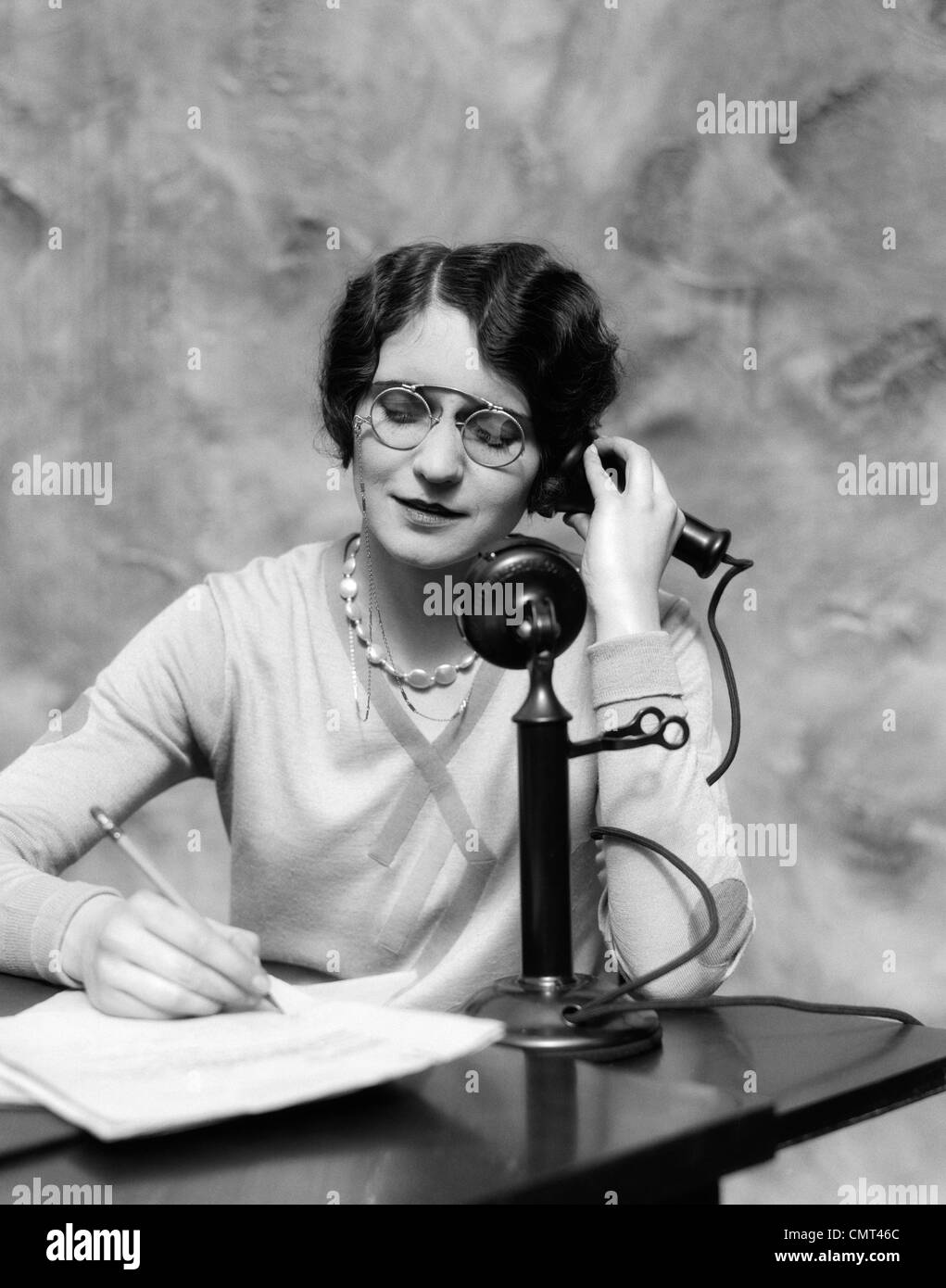 1920s WOMAN WEARING PINCE-NEZ GLASSES SITTING AT DESK TALKING ON  CANDLESTICK PHONE AND WRITING Stock Photo - Alamy
