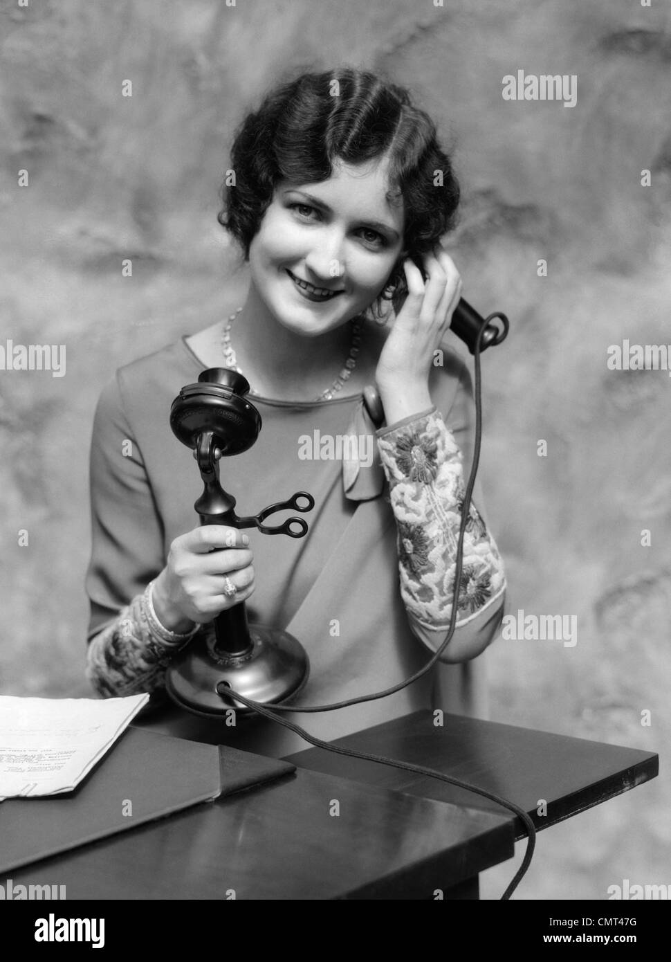 1920s PORTRAIT OF WOMAN ON CANDLESTICK TELEPHONE SMILING LOOKING AT CAMERA Stock Photo