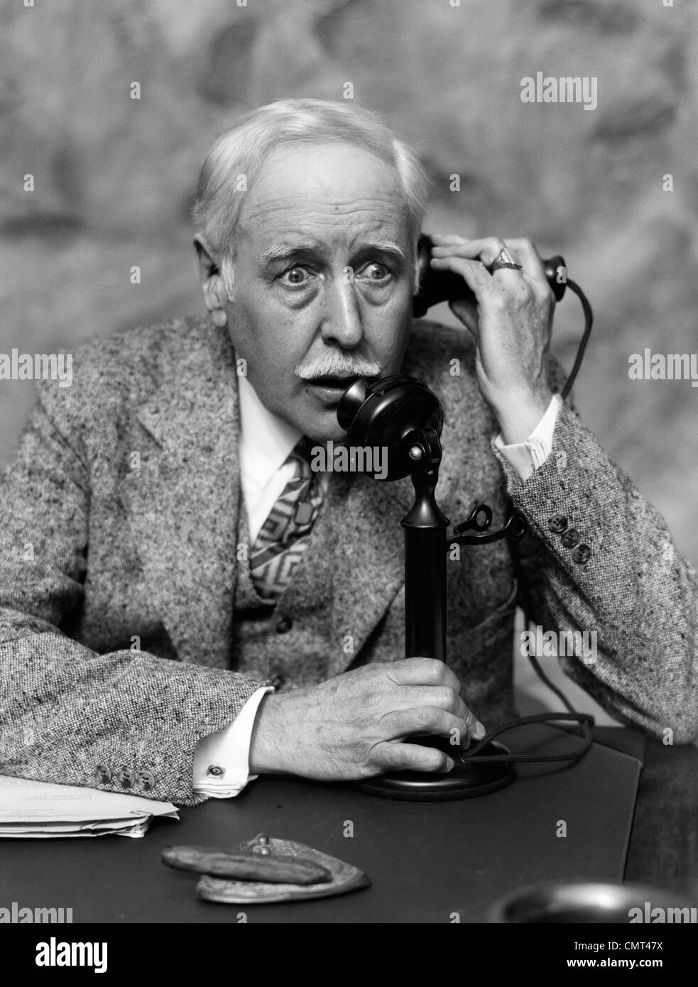 1920s 1930s BUSINESSMAN ON CANDLESTICK TELEPHONE LOOKING SURPRISED AND ALARMED Stock Photo