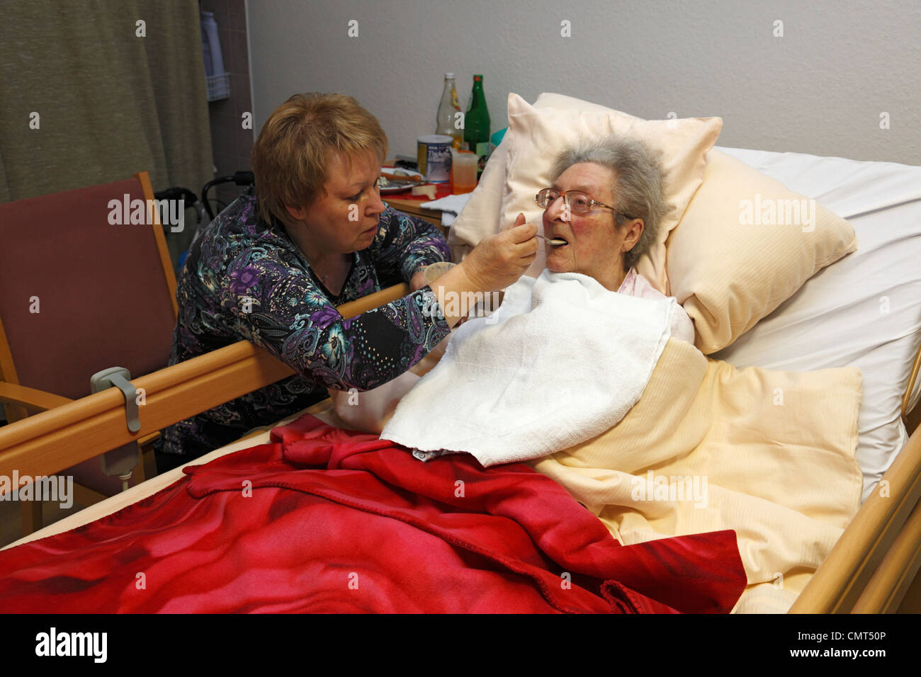 people, old age, retirement home, Altenzentrum der St. Clemens Hospitale in Sterkrade, older woman lies in a sickbed, aged 70 to 85 years, physical handicap, dementia illness, nurse feeds her, aged 50 to 60 years, Waltraut, Elke, D-Oberhausen, Ruhr area, Stock Photo