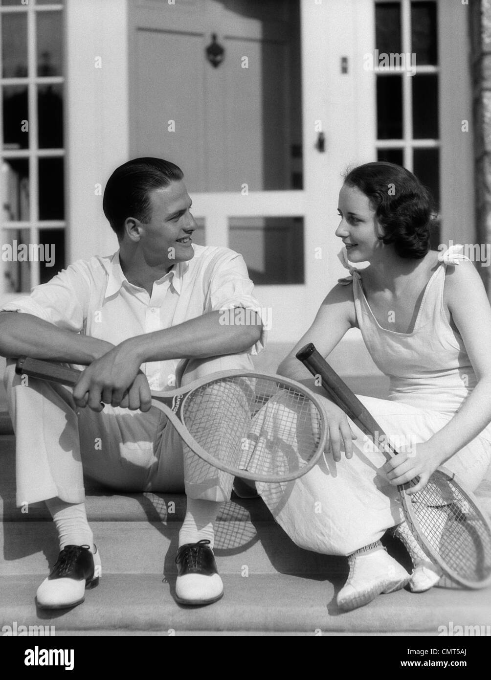 1930s COUPLE MAN WOMAN IN TENNIS WHITES HOLDING RACQUETS SITTING TALKING ON  STEPS IN FRONT OF HOUSE OUTDOOR Stock Photo - Alamy