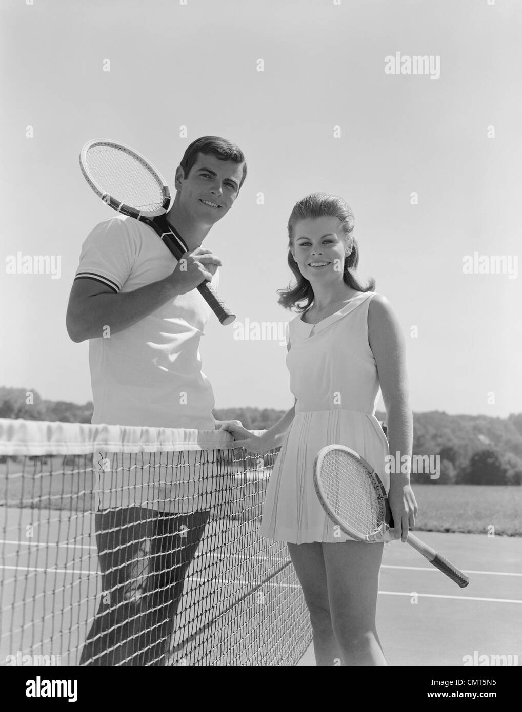 1960s PORTRAIT TENNIS COUPLE MAN WOMAN HOLDING RACQUETS STANDING BY NET Stock Photo
