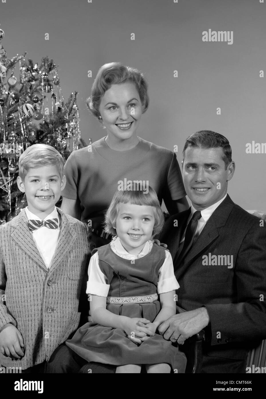 1950s 1960s FAMILY PORTRAIT SMILING FATHER MOTHER DAUGHTER SON SITTING TOGETHER IN FRONT OF INDOOR CHRISTMAS TREE Stock Photo