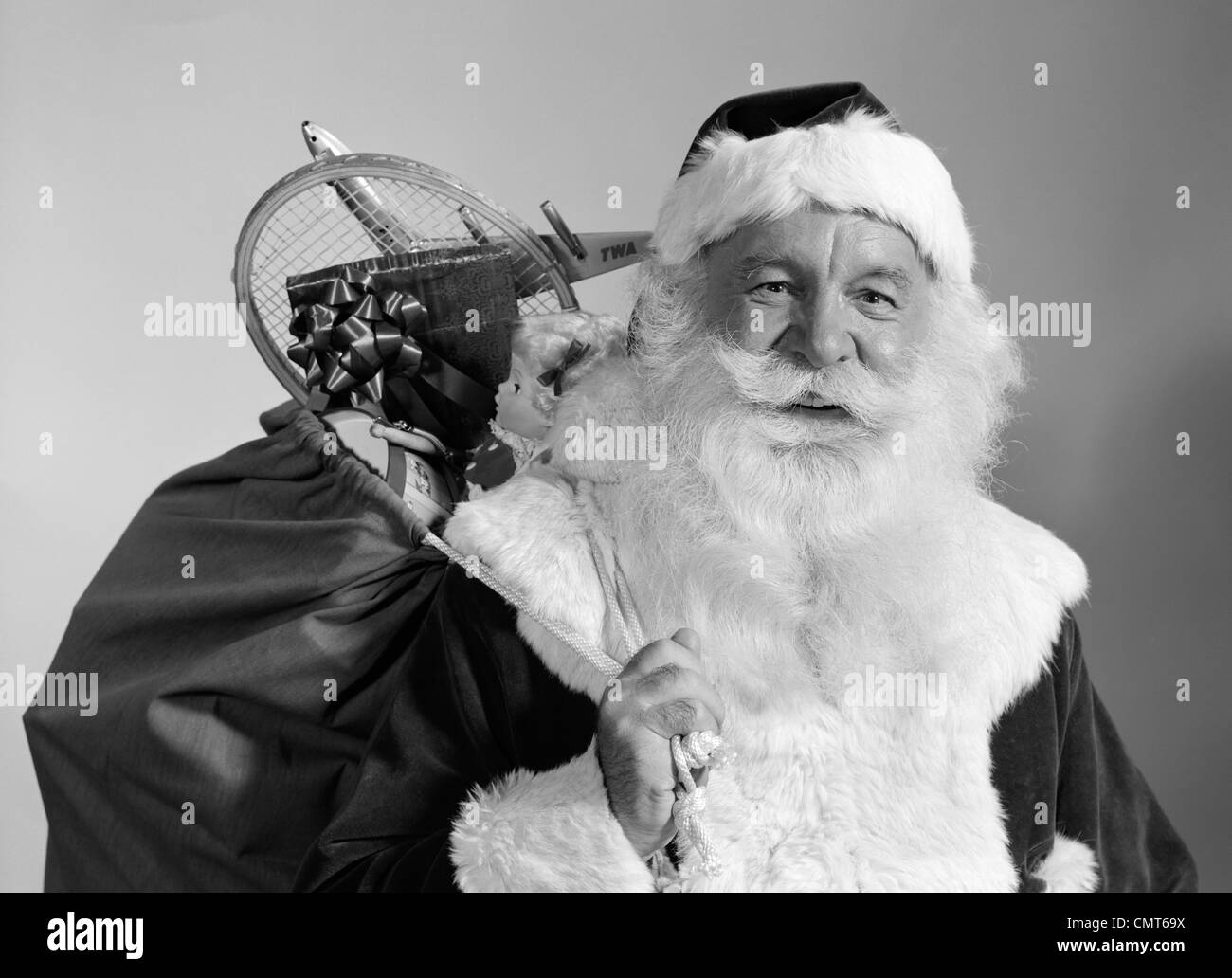 1960s PORTRAIT OF SMILING SANTA CLAUS WITH SACK OF CHRISTMAS TOY PRESENTS SLUNG OVER HIS SHOULDER Stock Photo