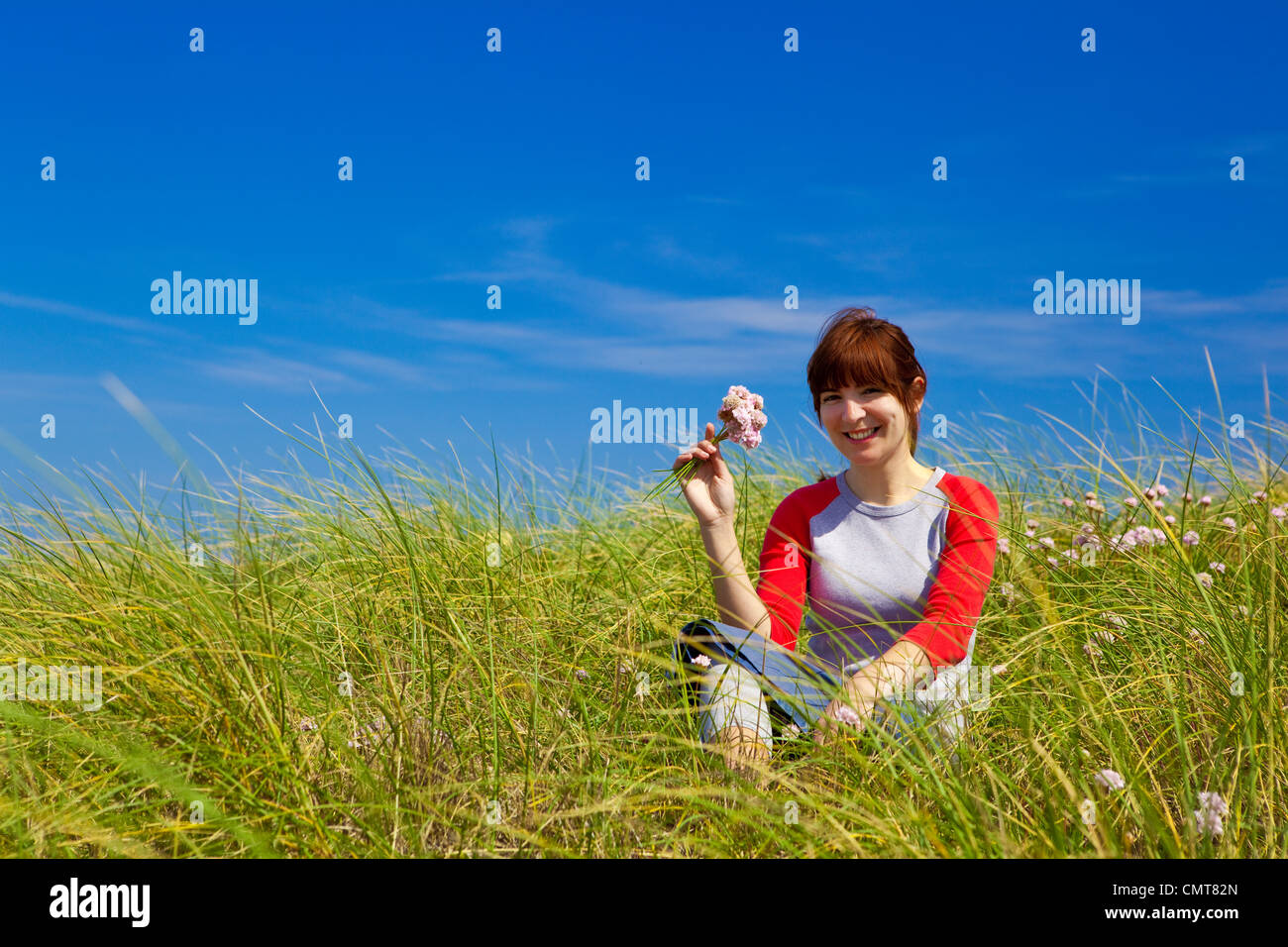 Happy woman sitting on a green meadow and holding flowers Stock Photo ...