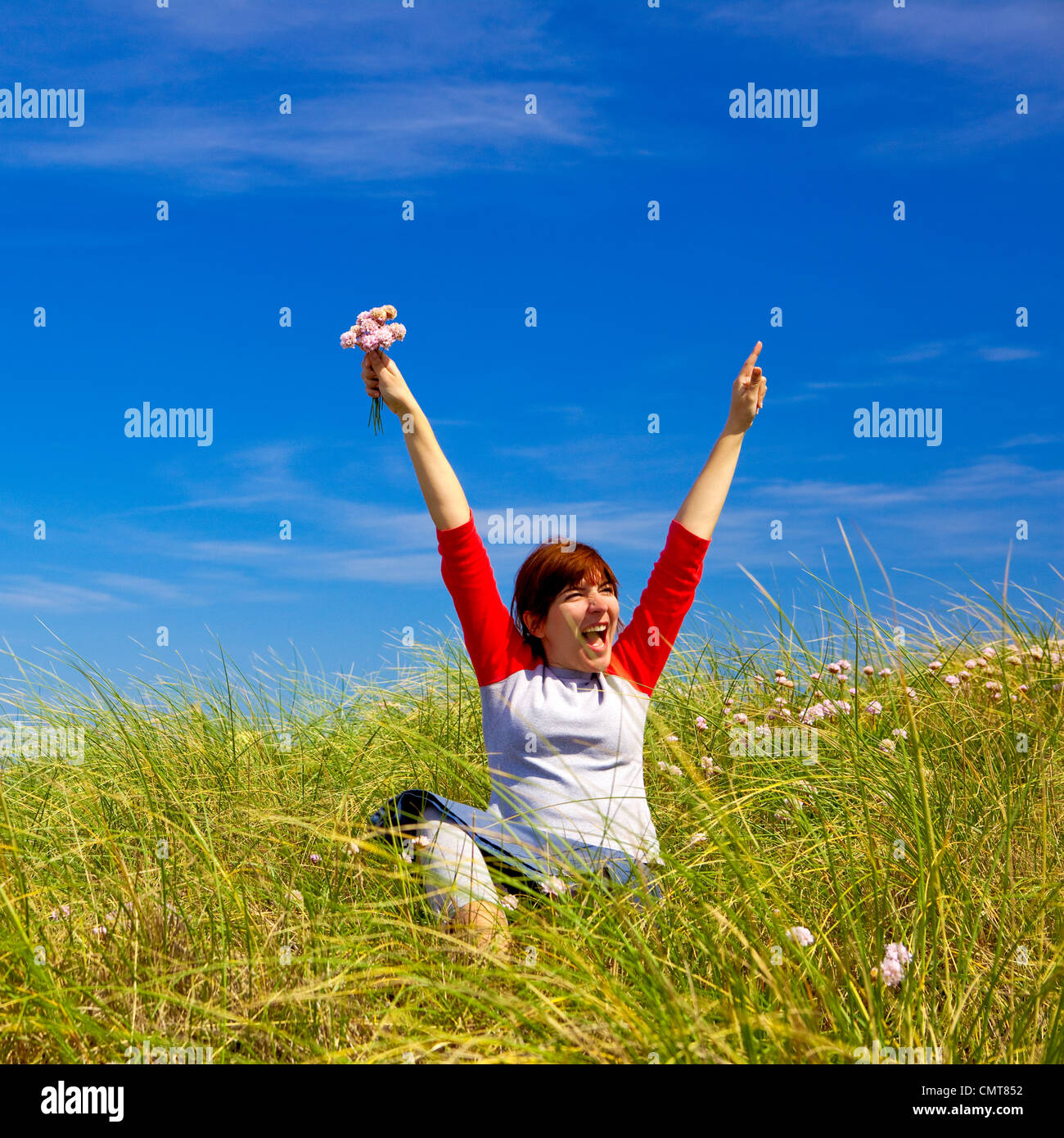 Happy woman sitting on a green meadow and holding flowers Stock Photo ...