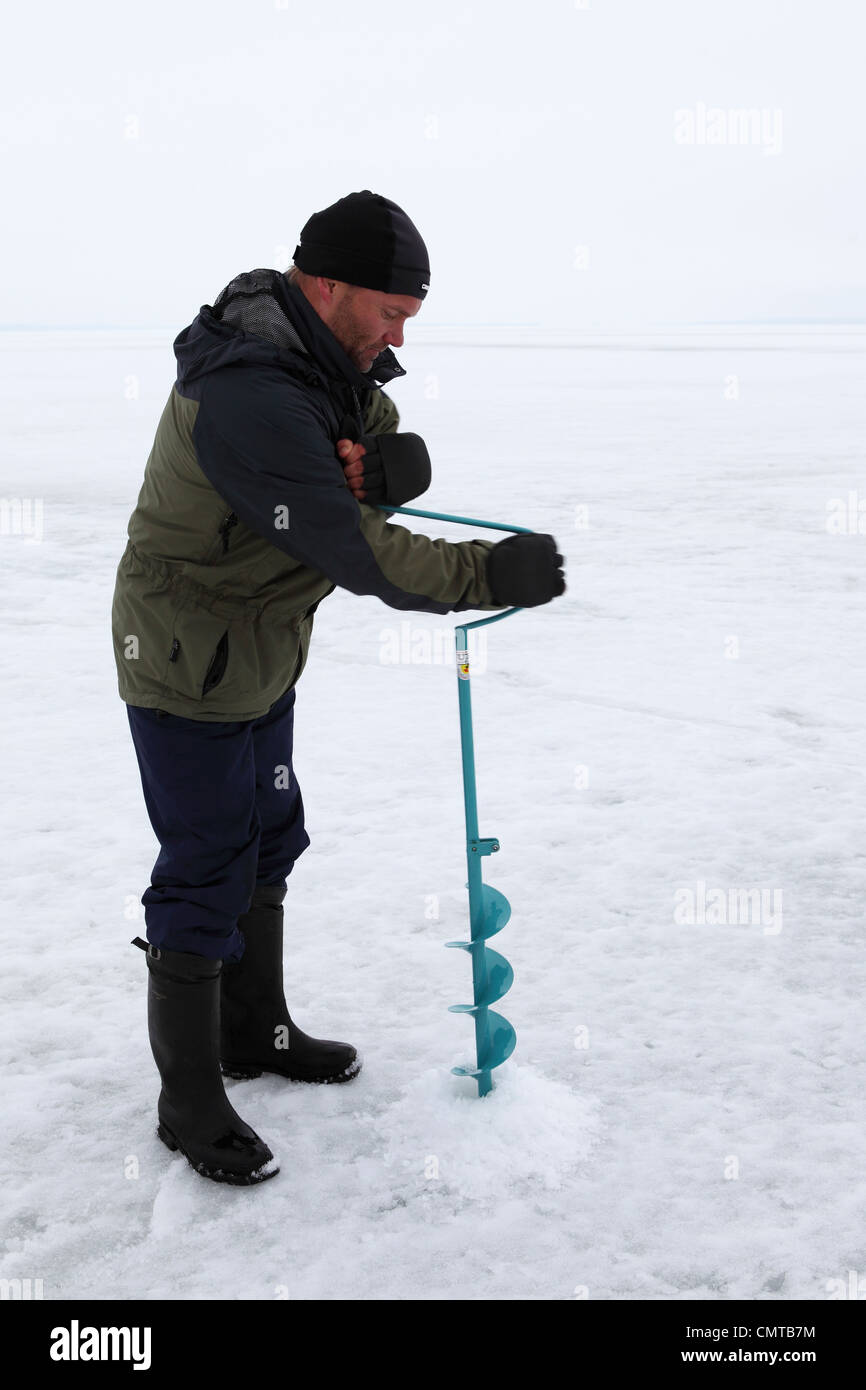 A man going icefishing drills a hole into the surface of Lake