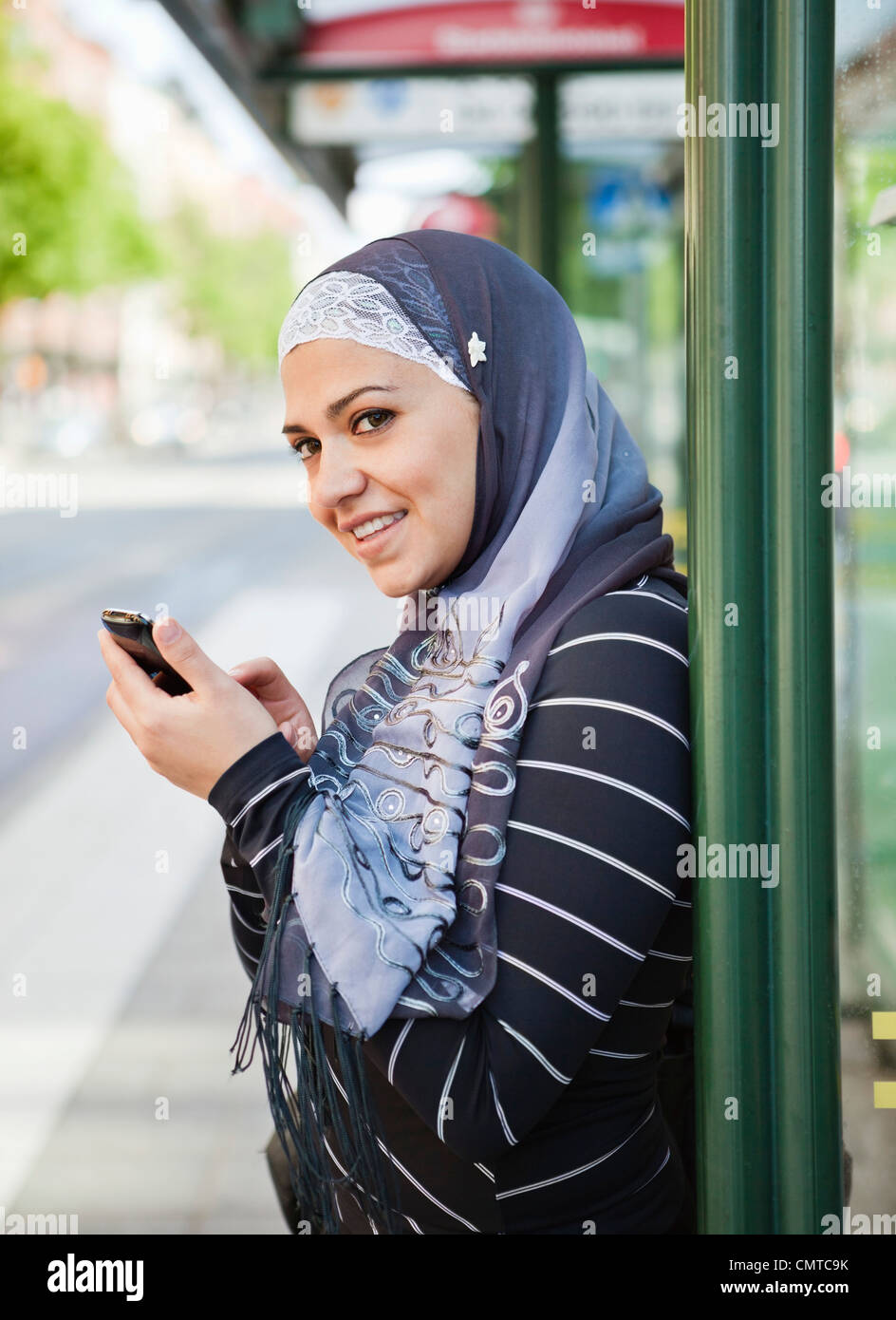 Smiling woman wearing headscarf waiting on bus Stock Photo