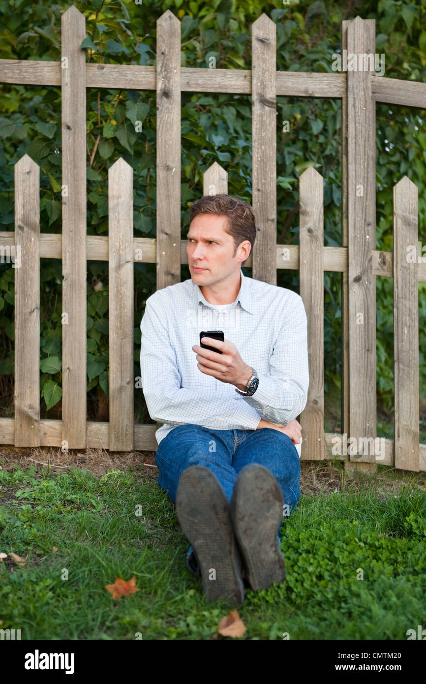 Man leaning against fence with cell phone in his hand Stock Photo