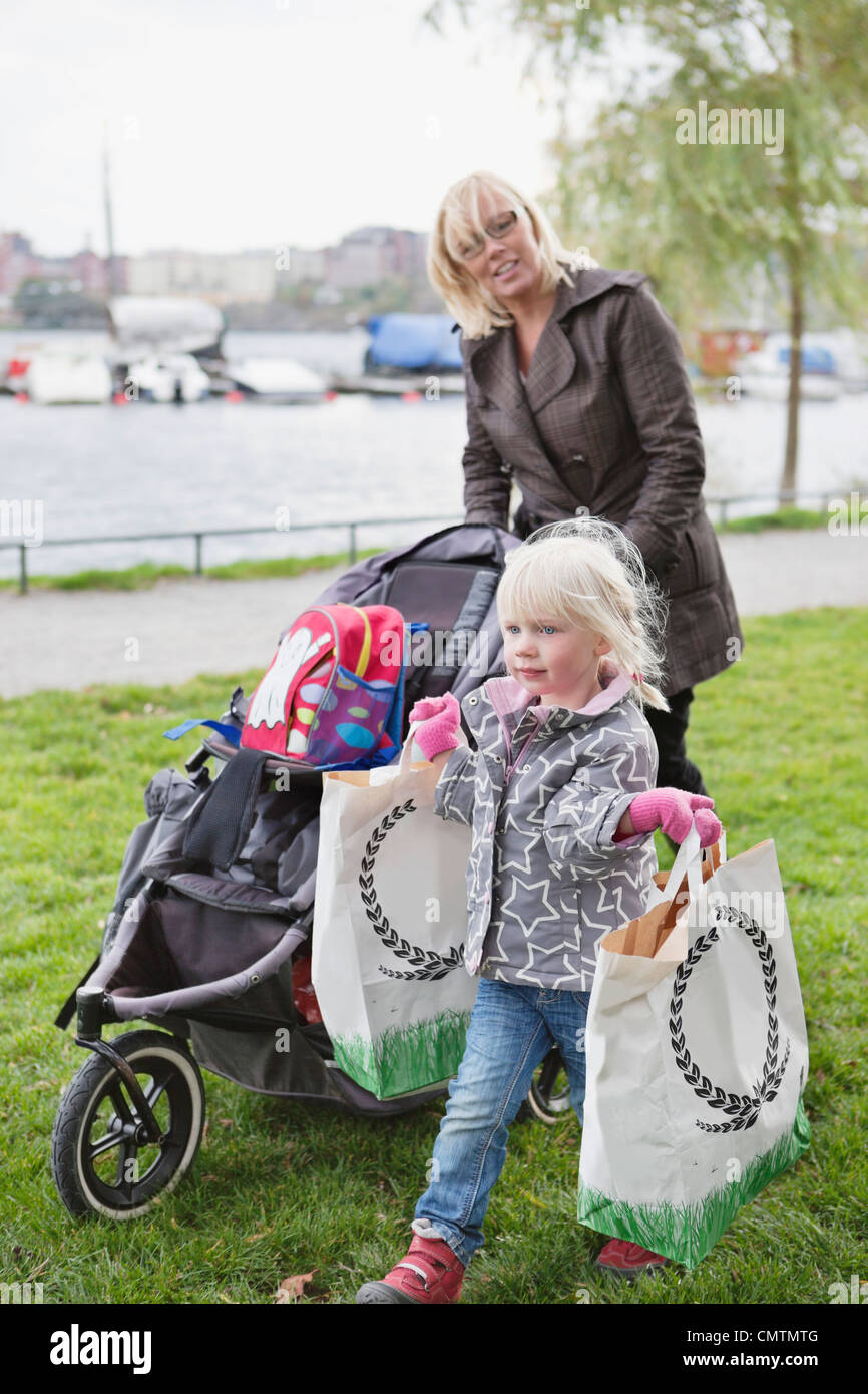 Child carrying bags while woman pushing cart Stock Photo