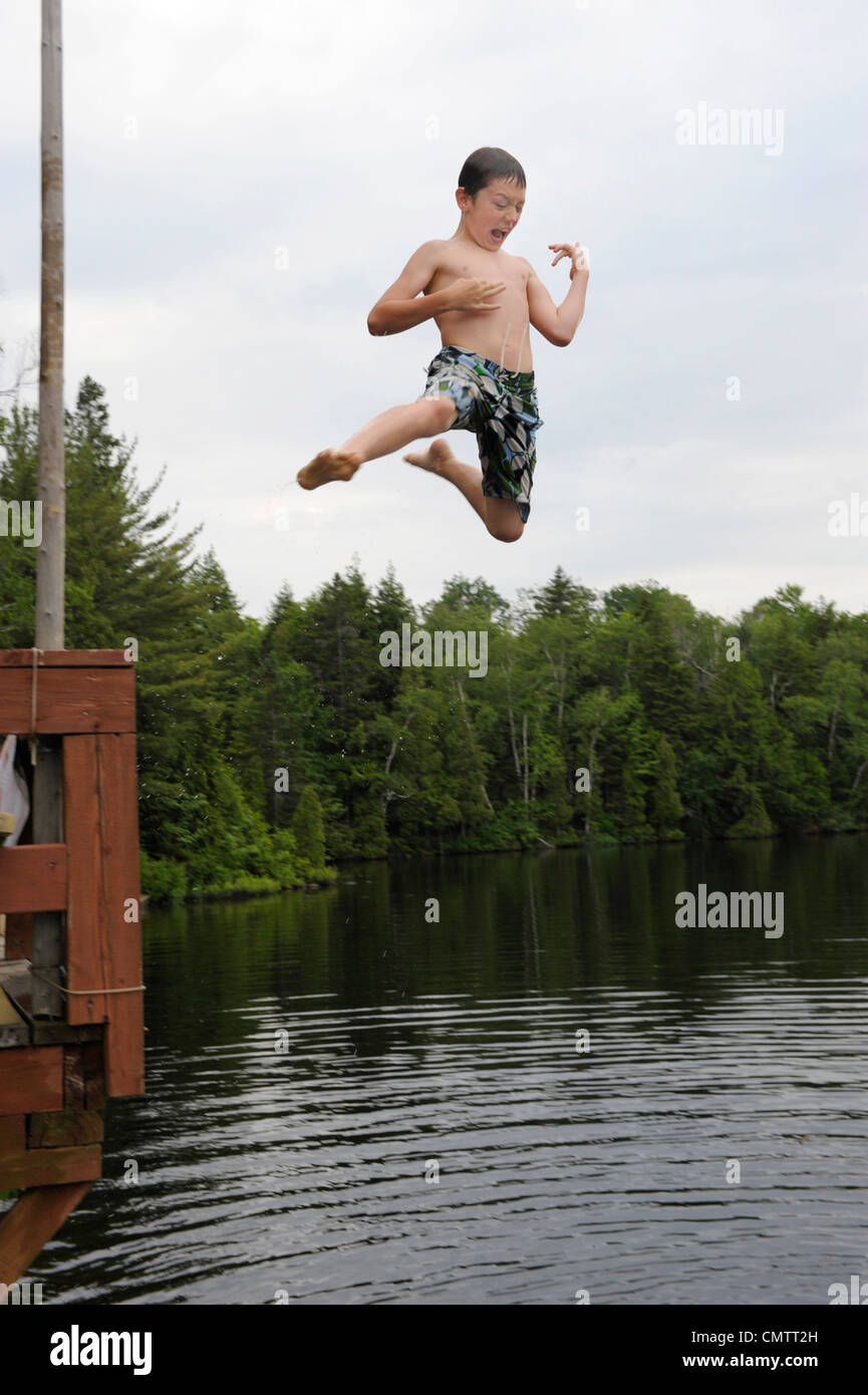 Boy playing air guitar while jumping off deck into Lac des Neiges, near Shawinigan, Quebec Stock Photo
