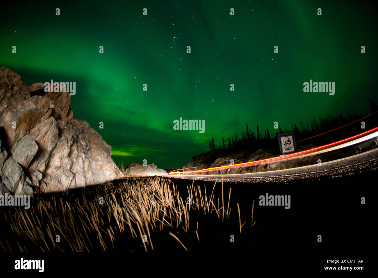 Lights of a passing vehicles under Aurora Borealis at the start of the Ingraham Trail, outside Yellowknife, NWT Stock Photo