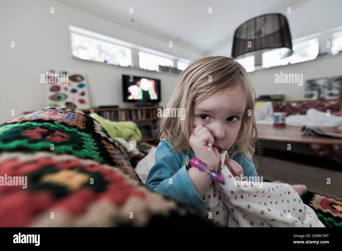 Blond haired girl sucking thumb while resting on sofa Stock Photo