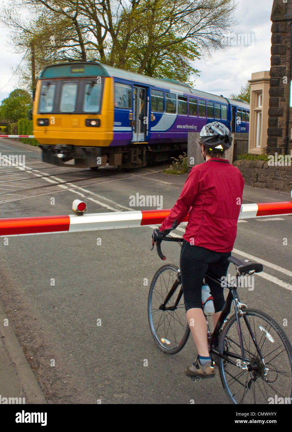 Woman cyclist waiting for train at level crossing near Burscough in West Lancashire Stock Photo