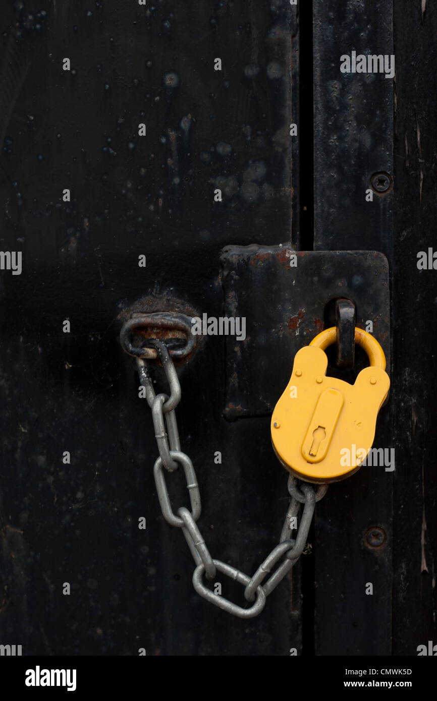 Yellow padlock and chain locking a heavy black door Stock Photo