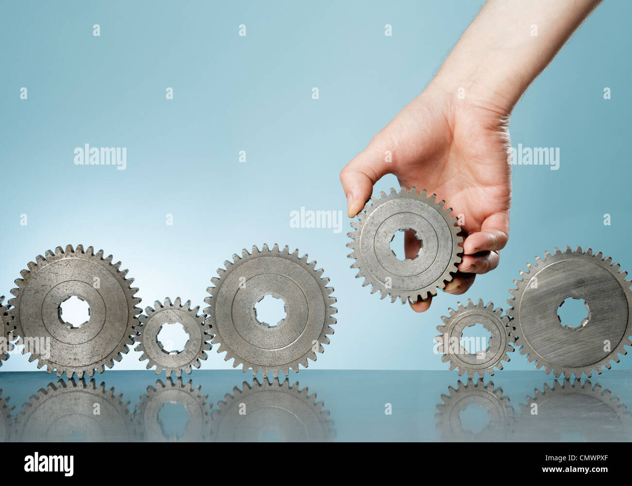 Man adding a cog gear in a row of old cog gears Stock Photo Alamy