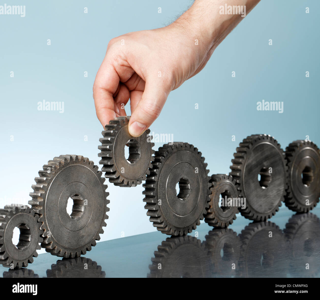 Man adding a cog gear in a row of old cog gears Stock Photo Alamy