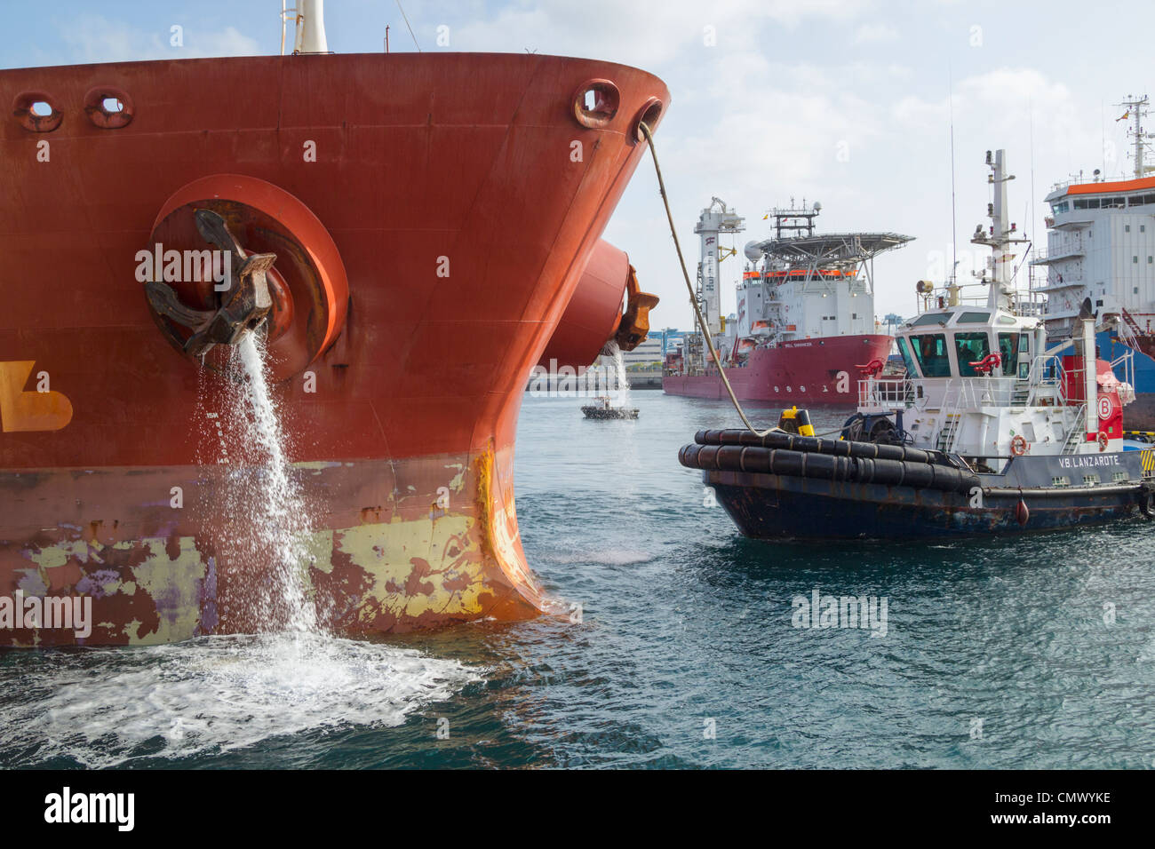 Oil tanker pumping ballast water as tug boat guides ship onto berth in port in Las Palmas, Gran Canaria Stock Photo