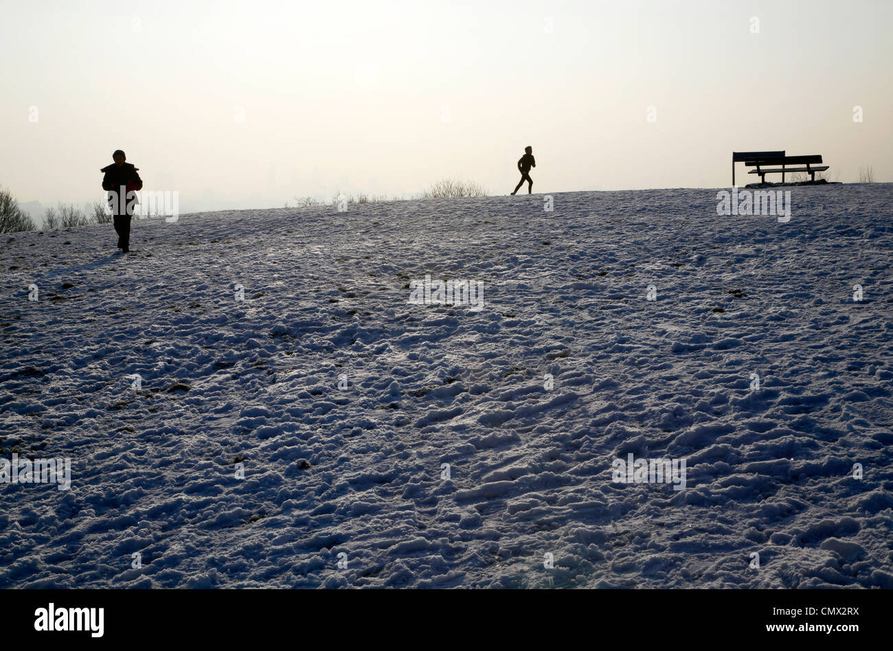 Walker and jogger taking in the view from the top of a snowy Parliament Hill, Hampstead Heath, London, UK Stock Photo